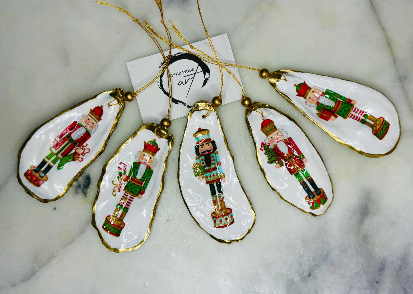 Handmade Nutcracker oyster shell Christmas ornaments with gold gilded edges and glossy resin finish. Traditional festive Nutcracker designs on natural pearl Dorset oyster shells in red, green, aqua, blue and gold tones, styled as luxury coastal Christmas tree decorations.