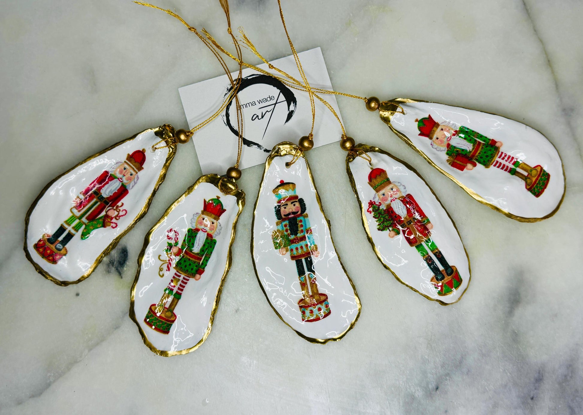 Handmade Nutcracker oyster shell Christmas ornaments with gold gilded edges and glossy resin finish. Traditional festive Nutcracker designs on natural pearl Dorset oyster shells in red, green, aqua, blue and gold tones, styled as luxury coastal Christmas tree decorations.