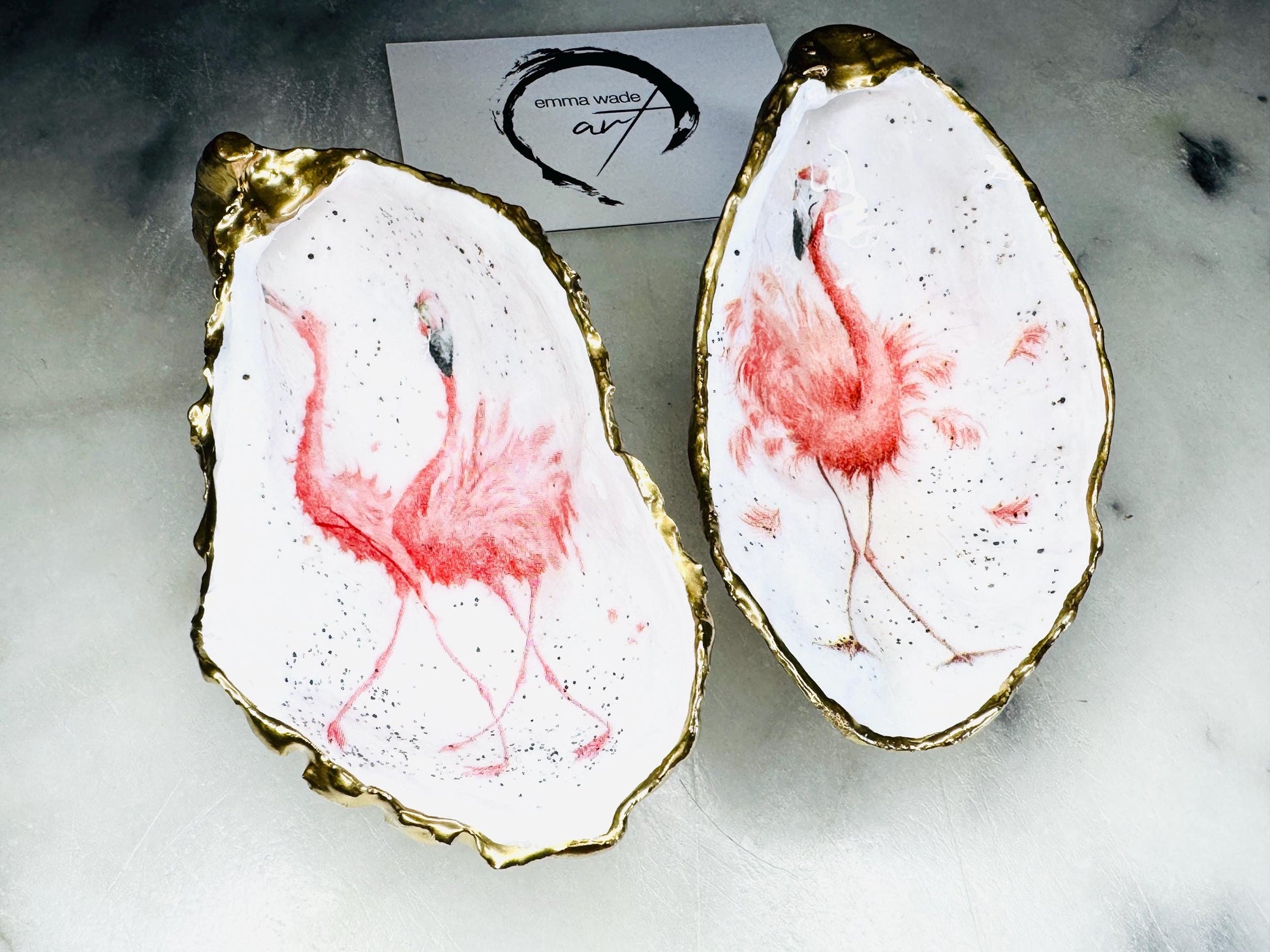 Handmade Dorset oyster shell trinket dishes featuring elegant pink flamingo bird artwork with hand-painted gold leaf edging and glossy crystal clear resin. Coastal flamingo jewellery holders styled on a white marble background with tropical blush pink tones and luxury coastal home décor styling.