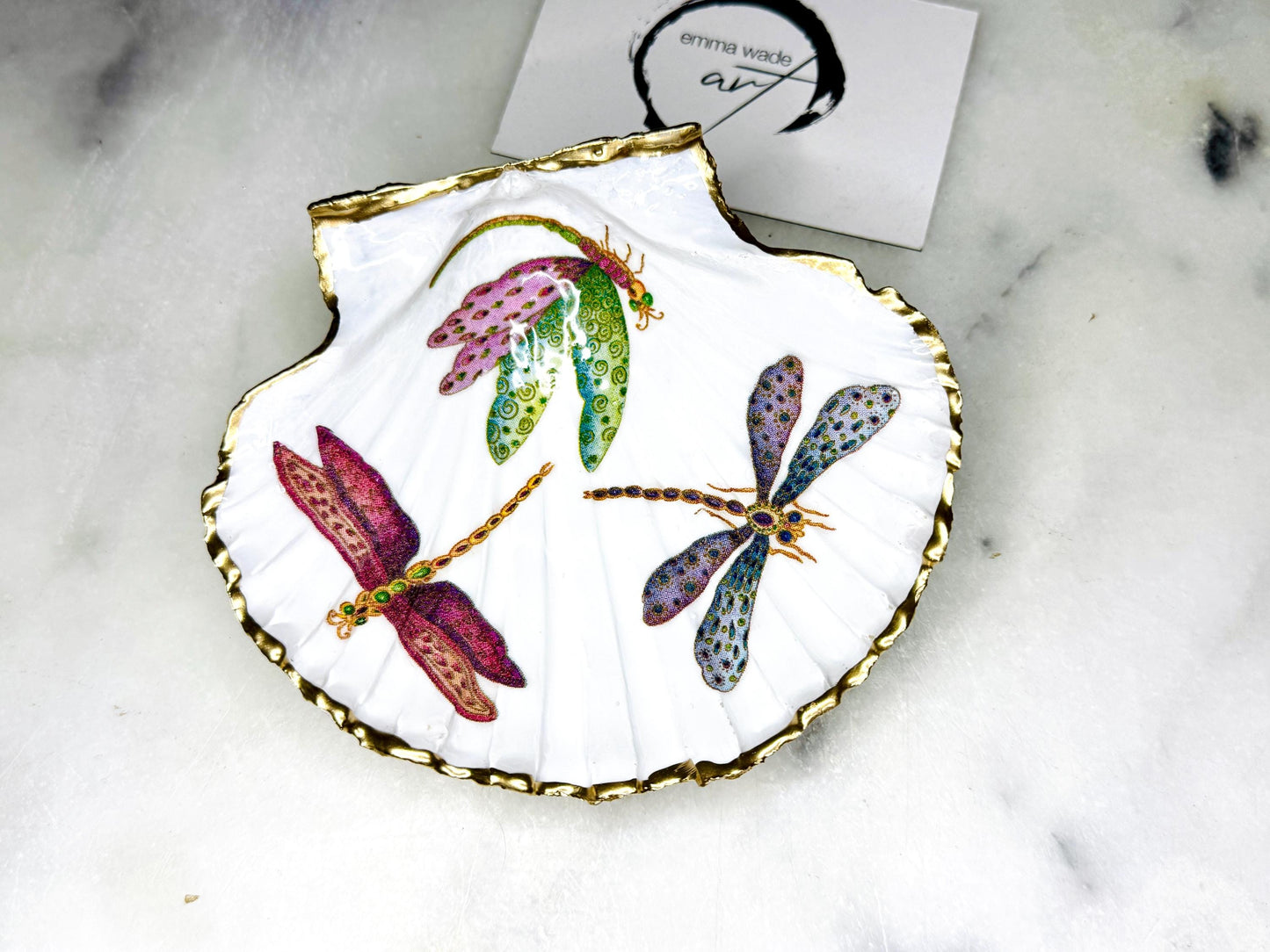 Handmade dragonfly scallop shell trinket dish with gold leaf edging and glossy resin finish. Coastal jewellery and ring dish crafted from a natural Dorset scallop shell, featuring colourful dragonfly artwork. Decorative shell bowl photographed on a light background, showing the natural shell shape and shimmering gilded edges, ideal for holding rings, earrings, trinkets or small treasures.