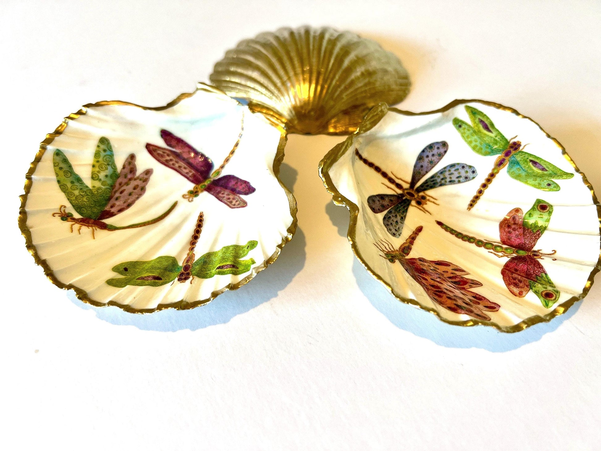 Handmade dragonfly scallop shell trinket dish with gold leaf edging and glossy resin finish. Coastal jewellery and ring dish crafted from a natural Dorset scallop shell, featuring colourful dragonfly artwork. Decorative shell bowl photographed on a light background, showing the natural shell shape and shimmering gilded edges, ideal for holding rings, earrings, trinkets or small treasures.