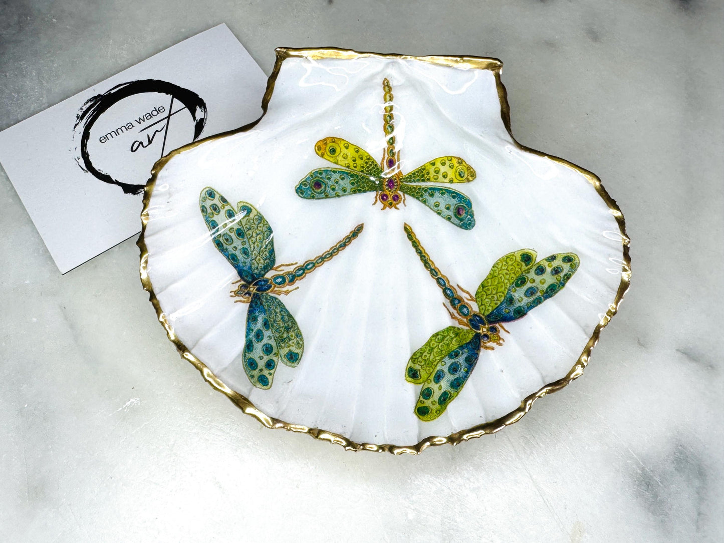 Handmade dragonfly scallop shell trinket dish with gold leaf edging and glossy resin finish. Coastal jewellery and ring dish crafted from a natural Dorset scallop shell, featuring colourful dragonfly artwork. Decorative shell bowl photographed on a light background, showing the natural shell shape and shimmering gilded edges, ideal for holding rings, earrings, trinkets or small treasures.