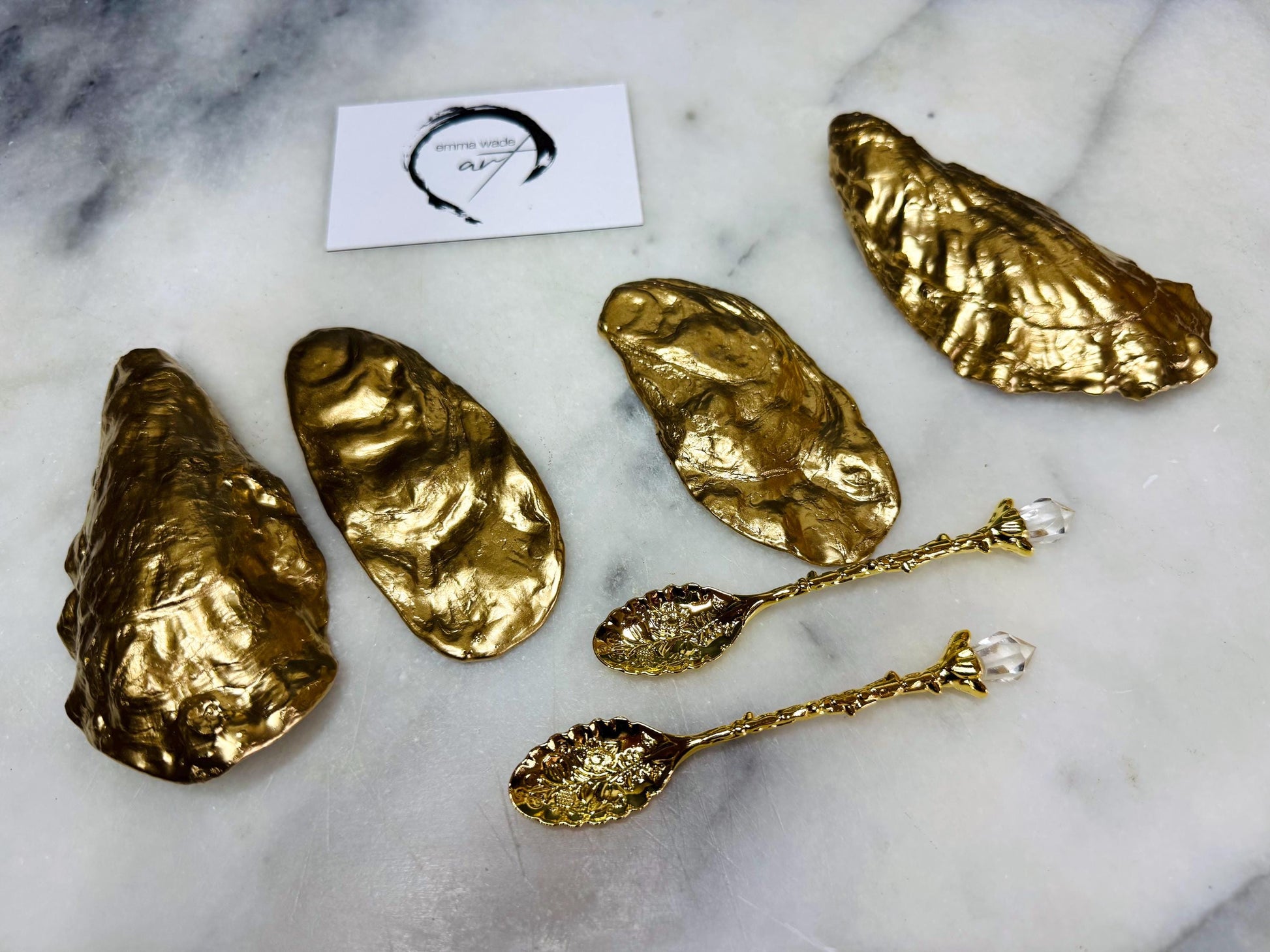 Handmade gold leaf oyster shell salt cellar set with pearl interiors and optional gold spoons. Coastal pinch pots made from natural Dorset oyster shells, sealed with food-safe glossy resin and finished with gilded edges. Luxury tableware set photographed on a light background, showing two shell salt dishes and matching spoons, ideal for serving salt, pepper or spices at dinner parties and stylish table settings. Gold leaf applied to backs of shells.