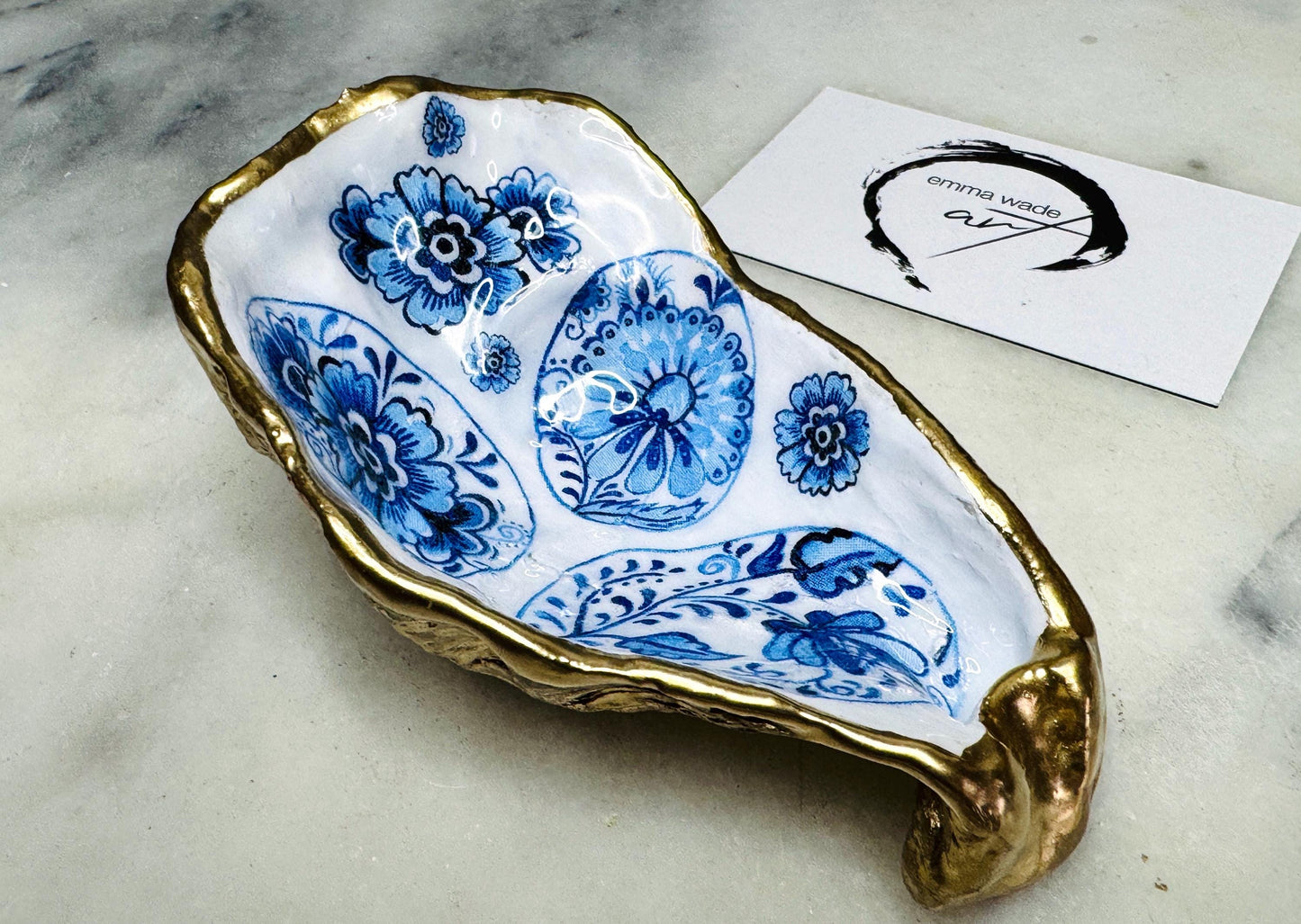Handmade Dorset oyster shell dish featuring a blue and white patterned egg design with vintage style detailing. Finished with real gold leaf and epoxy resin for durability. Unique oyster shell jewellery dish, trinket holder, salt and pepper pinch pot, tea light holder, or spoon rest. A coastal décor ornament and gift idea for birthdays, weddings, anniversaries, or Christmas. Sustainable handmade UK oyster shell art.