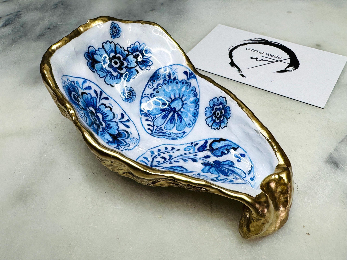Handmade Dorset oyster shell dish featuring a blue and white patterned egg design with vintage style detailing. Finished with real gold leaf and epoxy resin for durability. Unique oyster shell jewellery dish, trinket holder, salt and pepper pinch pot, tea light holder, or spoon rest. A coastal décor ornament and gift idea for birthdays, weddings, anniversaries, or Christmas. Sustainable handmade UK oyster shell art.