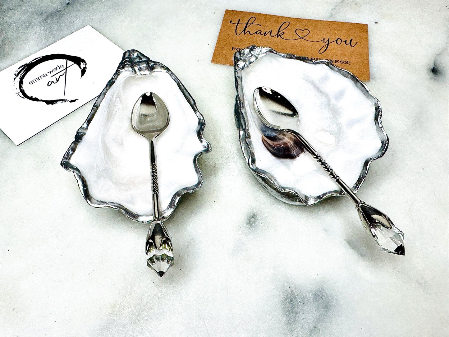 Handmade pearl oyster shell salt and pepper pinch pots with silver leaf accents and optional crystal spoons. Coastal tableware set made from natural Dorset oyster shells, polished to a natural white pearl finish and sealed with food-safe glossy resin. Elegant shell salt dishes photographed on a light background, showing two domed shells with matching bases, ideal for serving salt, pepper or spices at stylish dinner tables and special occasions.