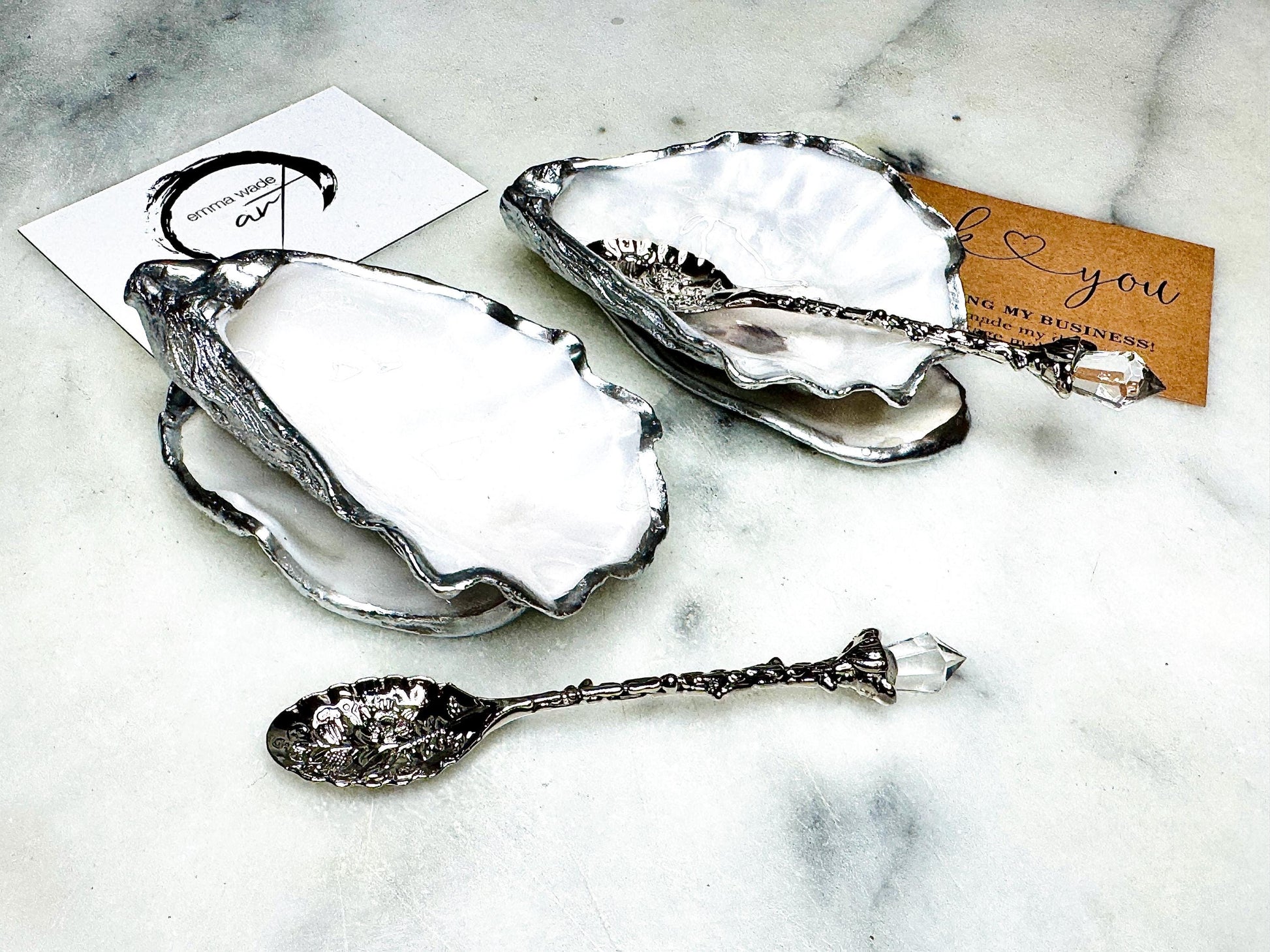 Handmade pearl oyster shell salt and pepper pinch pots with silver leaf accents and optional crystal spoons. Coastal tableware set made from natural Dorset oyster shells, polished to a natural white pearl finish and sealed with food-safe glossy resin. Elegant shell salt dishes photographed on a light background, showing two domed shells with matching bases, ideal for serving salt, pepper or spices at stylish dinner tables and special occasions.
