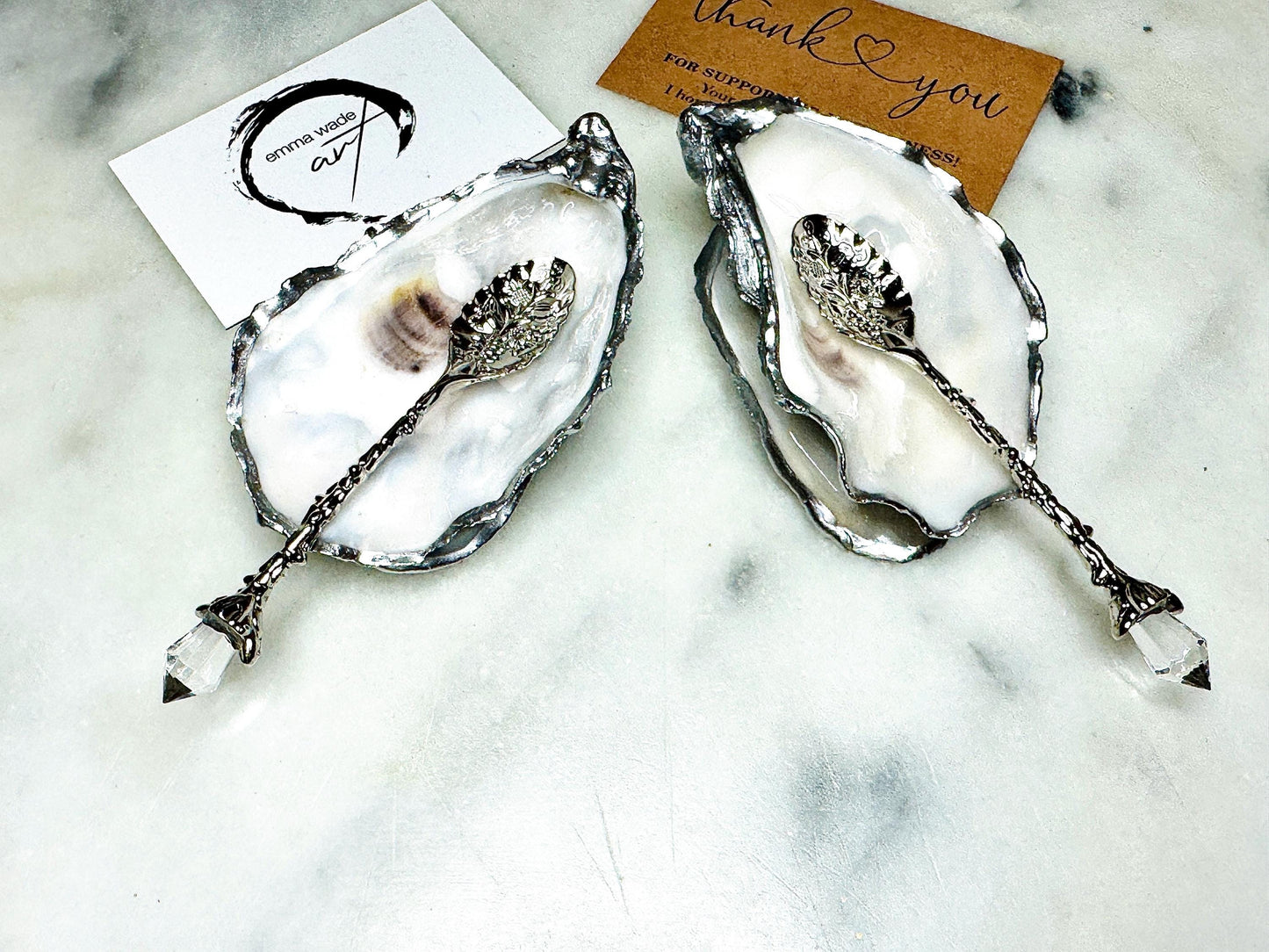 Handmade pearl oyster shell salt and pepper pinch pots with silver leaf accents and optional crystal spoons. Coastal tableware set made from natural Dorset oyster shells, polished to a natural white pearl finish and sealed with food-safe glossy resin. Elegant shell salt dishes photographed on a light background, showing two domed shells with matching bases, ideal for serving salt, pepper or spices at stylish dinner tables and special occasions.