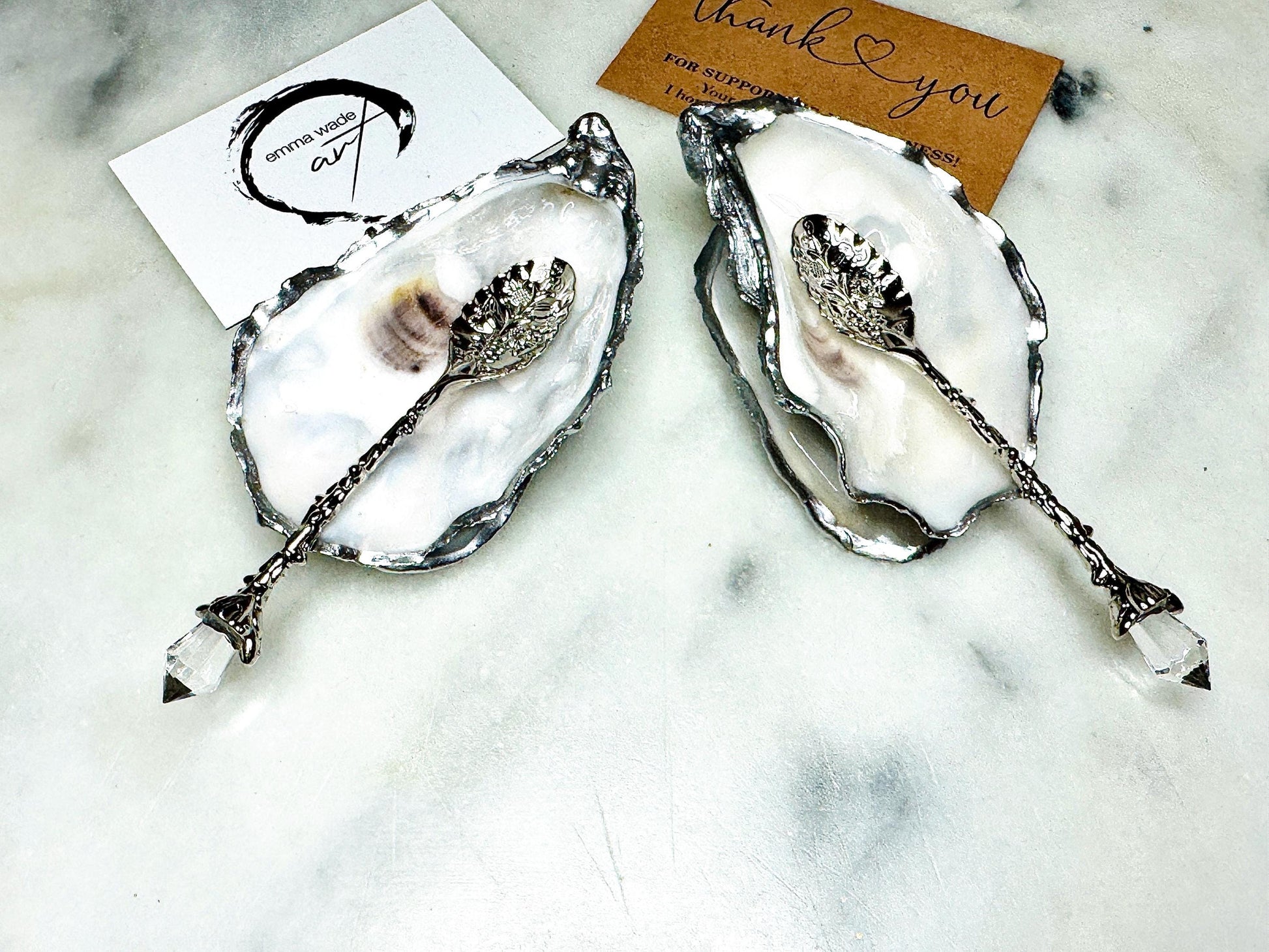 Handmade pearl oyster shell salt and pepper pinch pots with silver leaf accents and optional crystal spoons. Coastal tableware set made from natural Dorset oyster shells, polished to a natural white pearl finish and sealed with food-safe glossy resin. Elegant shell salt dishes photographed on a light background, showing two domed shells with matching bases, ideal for serving salt, pepper or spices at stylish dinner tables and special occasions.