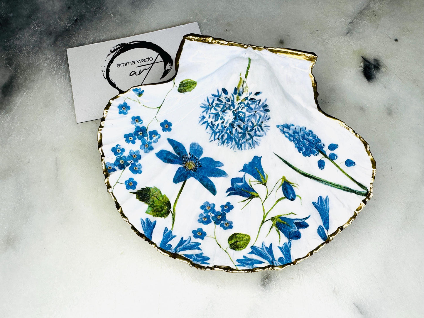 featuring delicate blue spring flowers including bluebells and forget-me-nots, finished with hand-applied gold leaf edging and glossy resin. Coastal shell ring holder and jewellery dish available in standard and large sizes, perfect for vanity décor, bridesmaid gifts, or elegant coastal home styling.