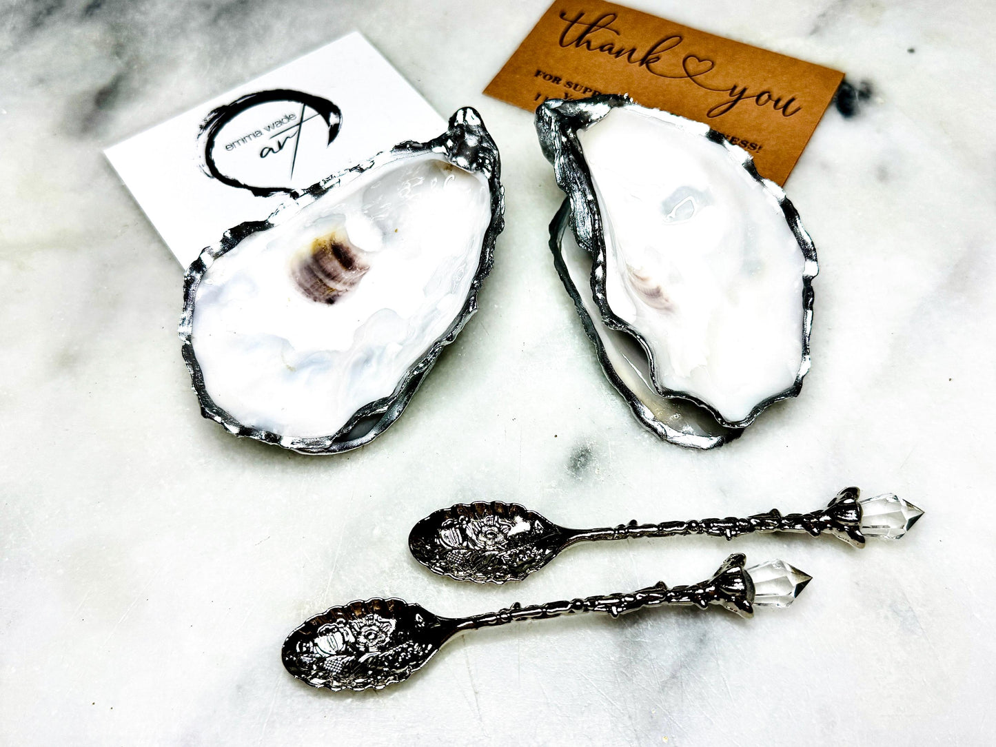 Handmade pearl oyster shell salt and pepper pinch pots with silver leaf accents and optional crystal spoons. Coastal tableware set made from natural Dorset oyster shells, polished to a natural white pearl finish and sealed with food-safe glossy resin. Elegant shell salt dishes photographed on a light background, showing two domed shells with matching bases, ideal for serving salt, pepper or spices at stylish dinner tables and special occasions.