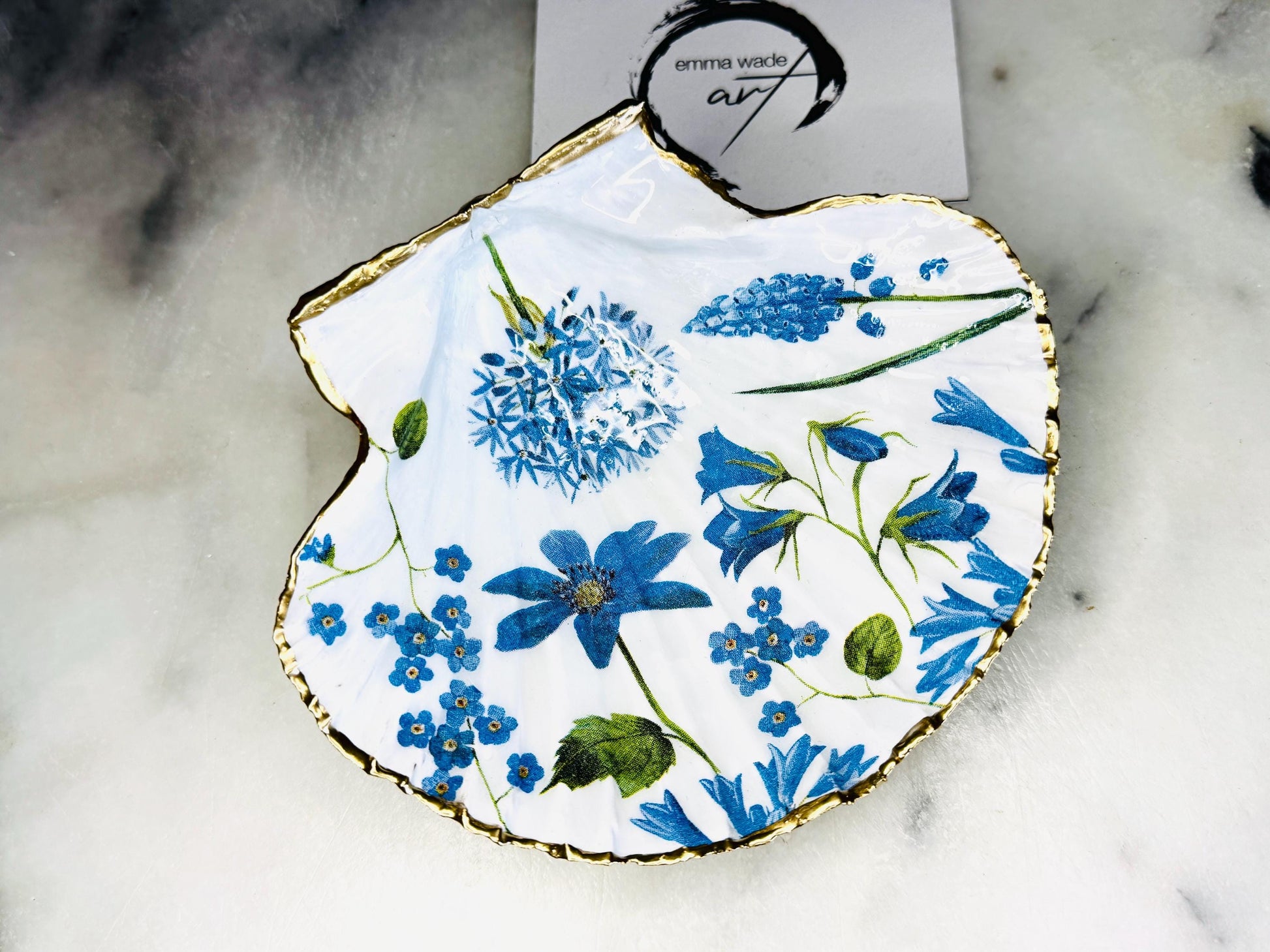 featuring delicate blue spring flowers including bluebells and forget-me-nots, finished with hand-applied gold leaf edging and glossy resin. Coastal shell ring holder and jewellery dish available in standard and large sizes, perfect for vanity décor, bridesmaid gifts, or elegant coastal home styling.