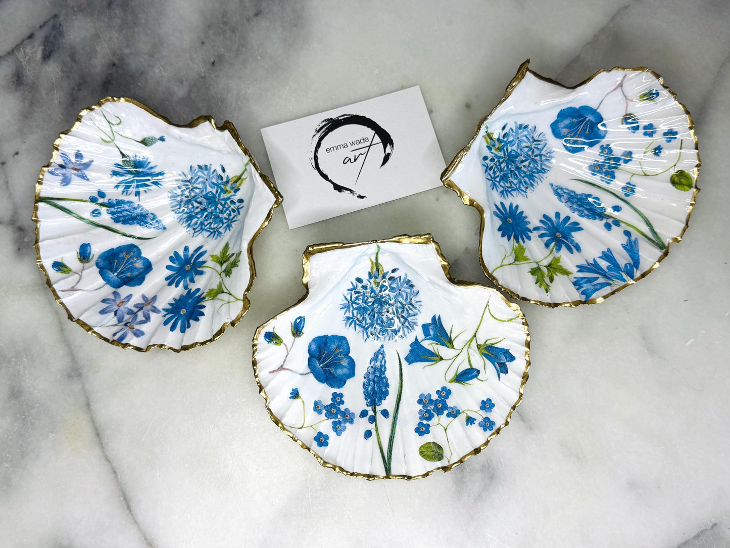 featuring delicate blue spring flowers including bluebells and forget-me-nots, finished with hand-applied gold leaf edging and glossy resin. Coastal shell ring holder and jewellery dish available in standard and large sizes, perfect for vanity décor, bridesmaid gifts, or elegant coastal home styling.