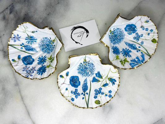 featuring delicate blue spring flowers including bluebells and forget-me-nots, finished with hand-applied gold leaf edging and glossy resin. Coastal shell ring holder and jewellery dish available in standard and large sizes, perfect for vanity décor, bridesmaid gifts, or elegant coastal home styling.