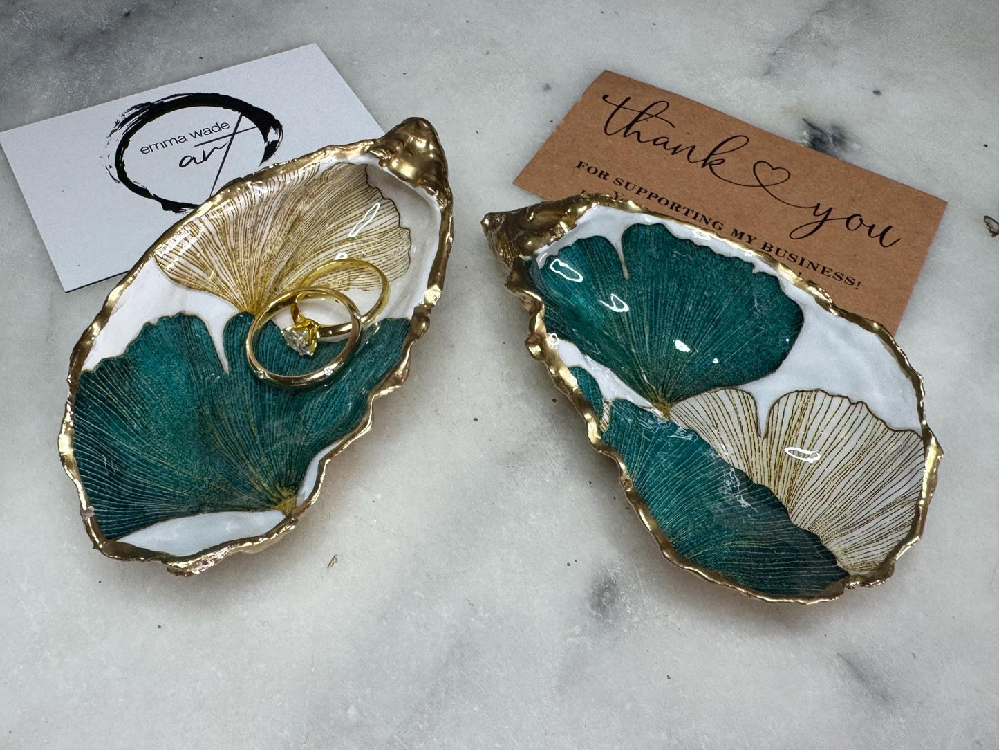 Handmade Dorset oyster shell ring dish featuring Japanese Ginkgo floral leaf artwork in emerald green, gold, and pearl tones with hand-applied liquid gold leaf edging. Luxury coastal jewellery tray sealed in glossy crystal-clear epoxy resin, styled with gold rings.