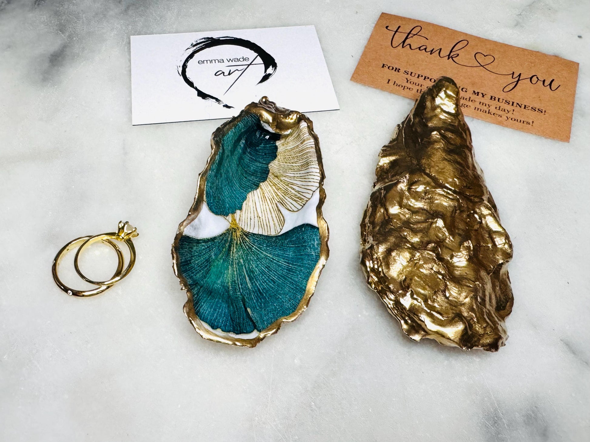 Handmade Dorset oyster shell ring dish featuring Japanese Ginkgo floral leaf artwork in emerald green, gold, and pearl tones with hand-applied liquid gold leaf edging. Luxury coastal jewellery tray sealed in glossy crystal-clear epoxy resin, styled with gold rings.