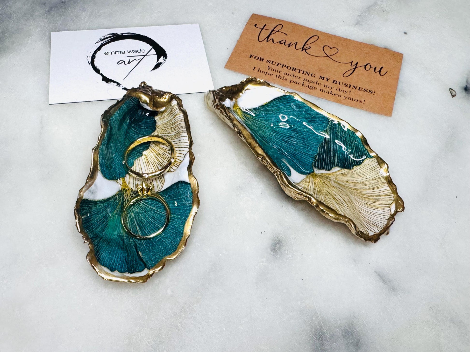 Handmade Dorset oyster shell ring dish featuring Japanese Ginkgo floral leaf artwork in emerald green, gold, and pearl tones with hand-applied liquid gold leaf edging. Luxury coastal jewellery tray sealed in glossy crystal-clear epoxy resin, styled with gold rings.