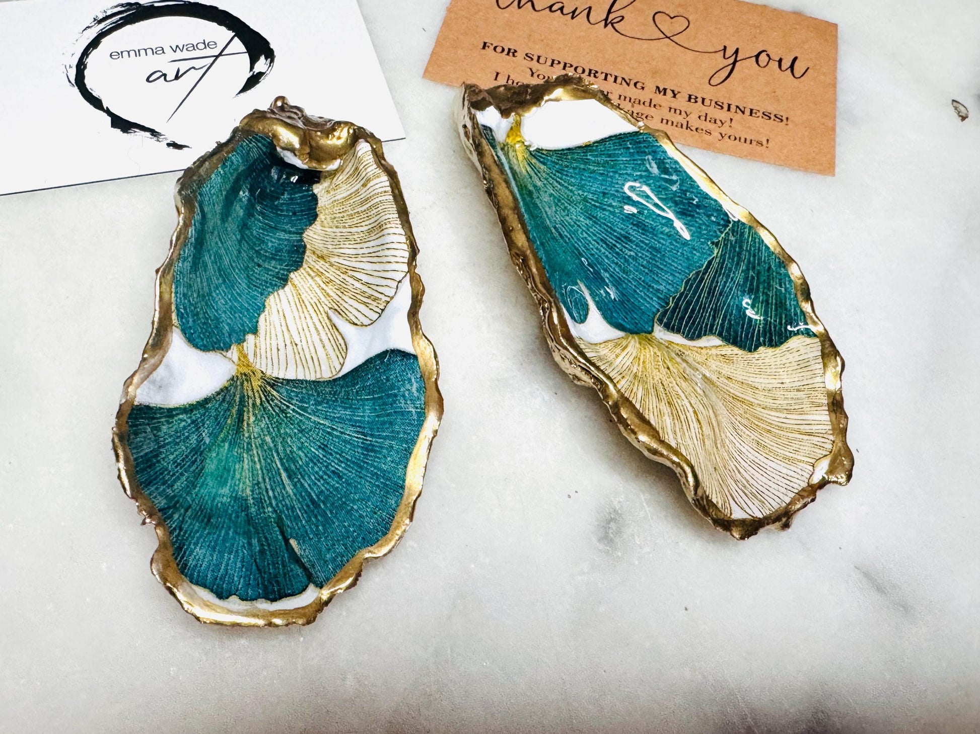 Handmade Dorset oyster shell ring dish featuring Japanese Ginkgo floral leaf artwork in emerald green, gold, and pearl tones with hand-applied liquid gold leaf edging. Luxury coastal jewellery tray sealed in glossy crystal-clear epoxy resin, styled with gold rings.
