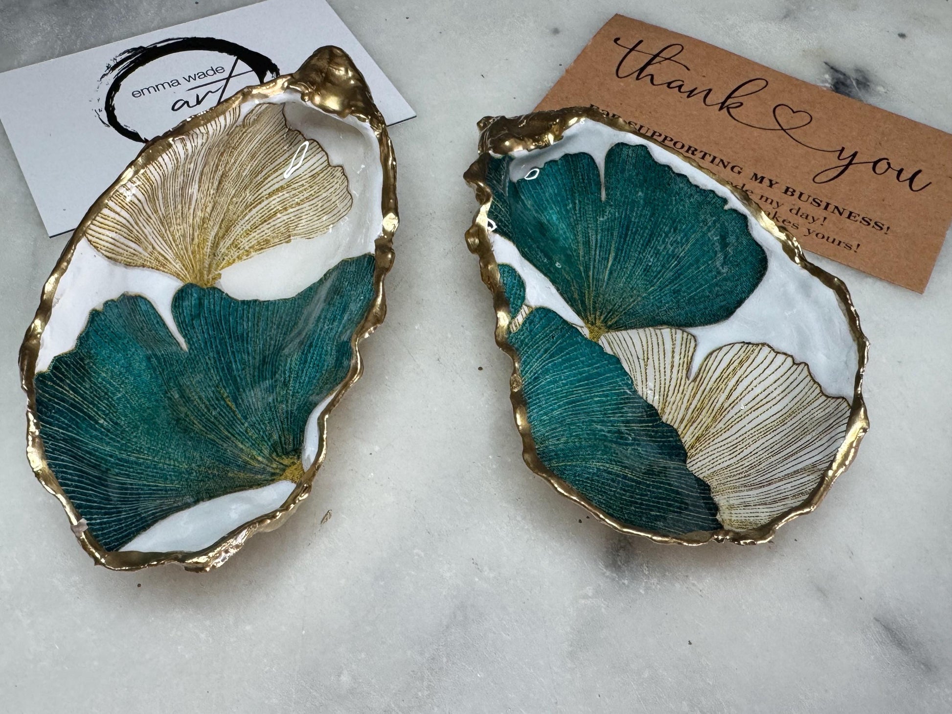 Handmade Dorset oyster shell ring dish featuring Japanese Ginkgo floral leaf artwork in emerald green, gold, and pearl tones with hand-applied liquid gold leaf edging. Luxury coastal jewellery tray sealed in glossy crystal-clear epoxy resin, styled with gold rings.