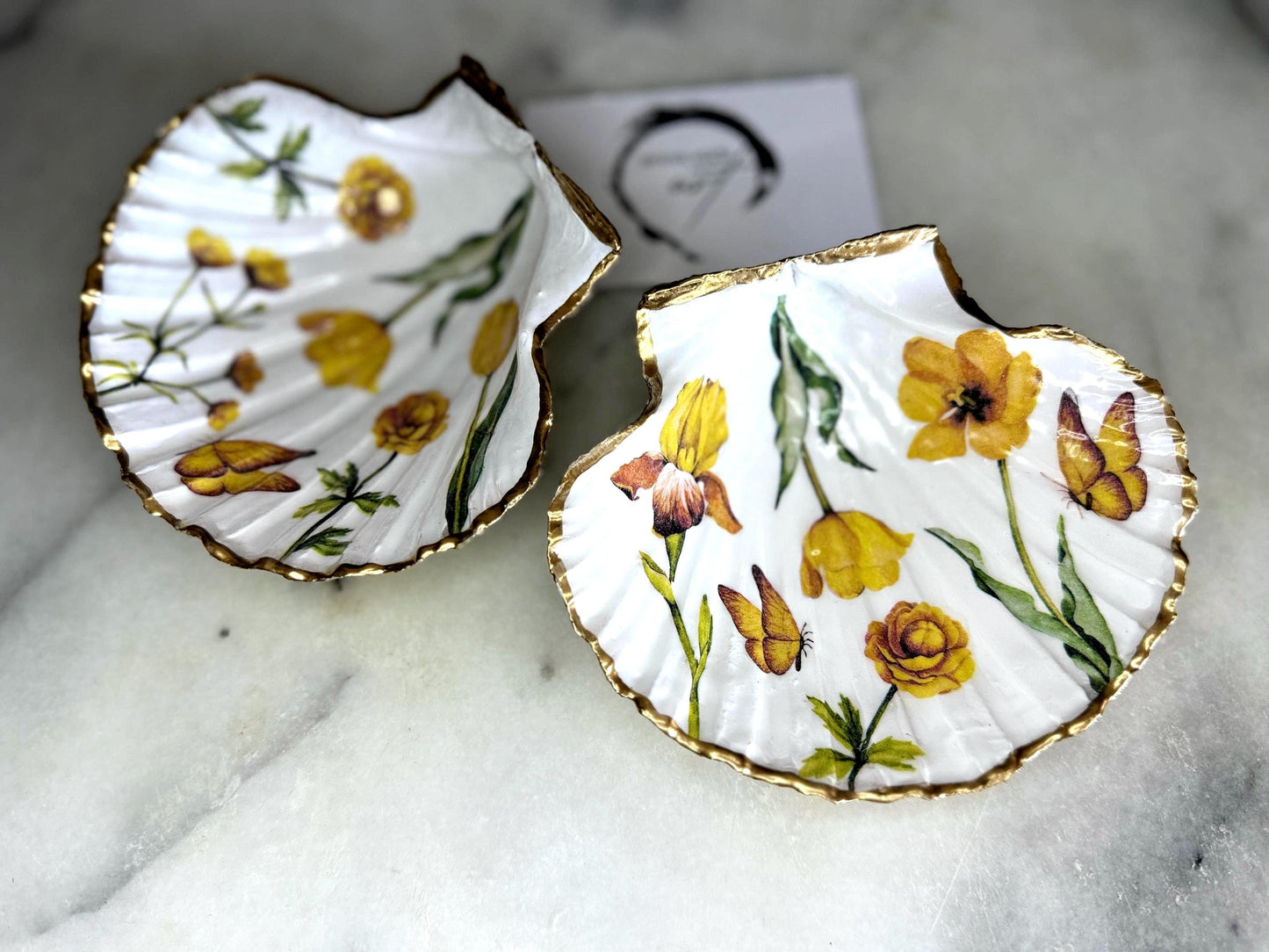 Hand finished scallop shell trinket dish featuring yellow spring flower artwork with a hand gilded gold leaf rim, sealed in glossy clear resin for durability and shine. Coastal inspired shell jewellery dish photographed on a light surface, ideal for rings, earrings and small keepsakes. Decorative floral shell dish by EmmaWadeART inspired by the Dorset coastline, perfect as a gift or elegant home décor accent.