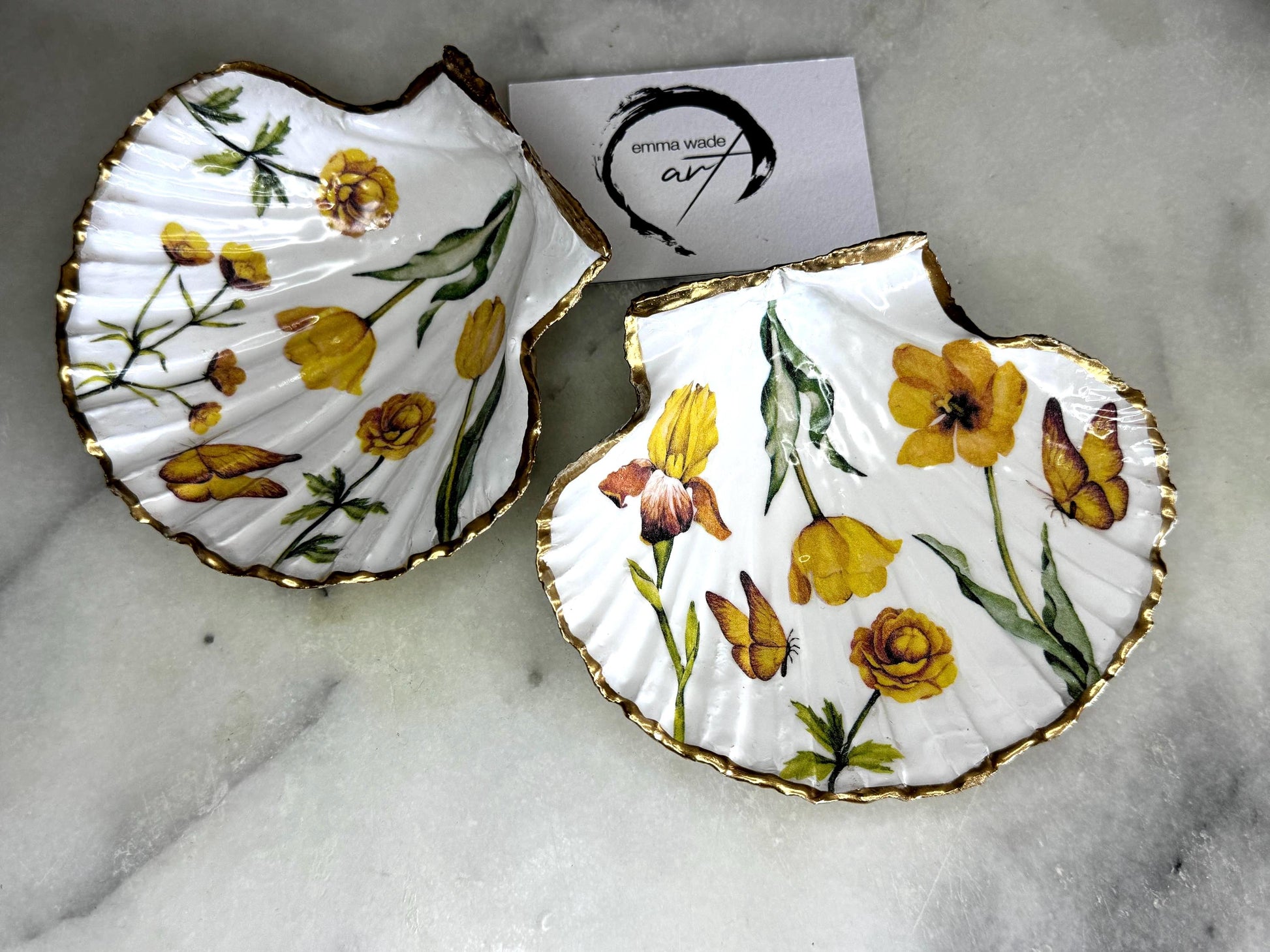 Hand finished scallop shell trinket dish featuring yellow spring flower artwork with a hand gilded gold leaf rim, sealed in glossy clear resin for durability and shine. Coastal inspired shell jewellery dish photographed on a light surface, ideal for rings, earrings and small keepsakes. Decorative floral shell dish by EmmaWadeART inspired by the Dorset coastline, perfect as a gift or elegant home décor accent.