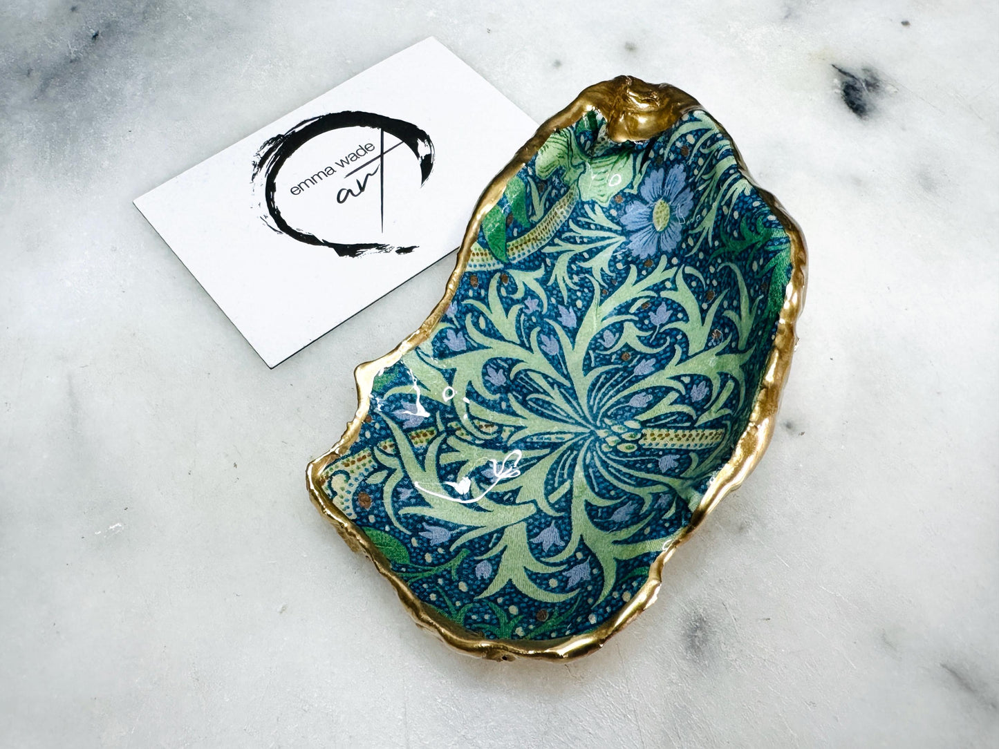 Handmade William Morris inspired oyster shell trinket dish in green and blue tones, finished with gold leaf and sealed with glossy resin. Coastal jewellery dish made from a Dorset oyster shell, featuring a seaweed decoupage design. Perfect for holding rings, earrings and small treasures. Decorative shell bowl photographed on a light background, showing the natural shell shape, detailed pattern and gilded edges.