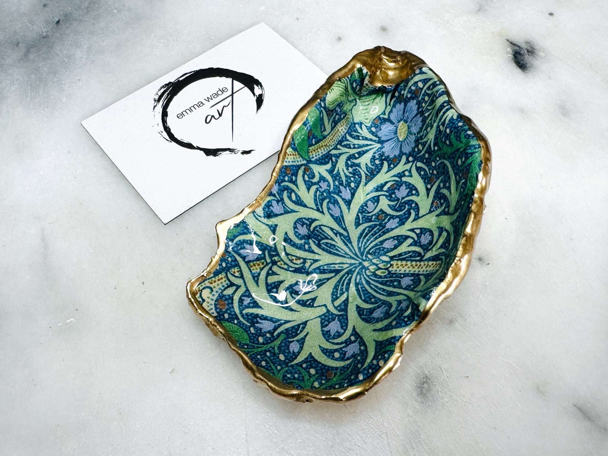 Handmade William Morris inspired oyster shell trinket dish in green and blue tones, finished with gold leaf and sealed with glossy resin. Coastal jewellery dish made from a Dorset oyster shell, featuring a seaweed decoupage design. Perfect for holding rings, earrings and small treasures. Decorative shell bowl photographed on a light background, showing the natural shell shape, detailed pattern and gilded edges.