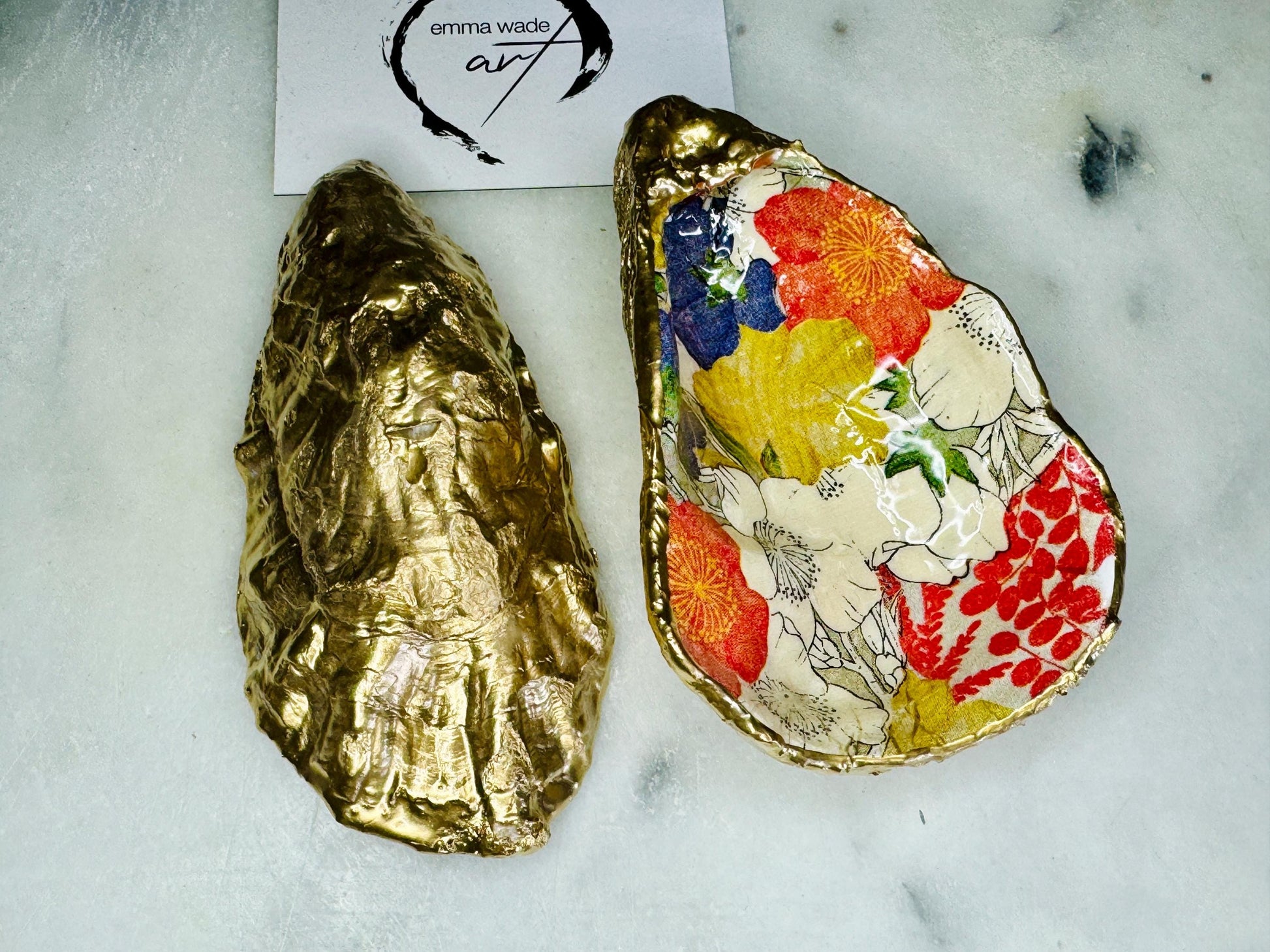 Handmade oyster shell trinket dish featuring a colourful Japanese kimono-style floral design applied with decoupage, finished with hand-gilded gold leaf edges and sealed in glossy clear resin. Natural Dorset oyster shell used as a jewellery dish or ring holder, photographed on a light surface, showcasing the vibrant flowers and luxury gold detailing. Ideal as coastal home decor or a unique handmade gift.