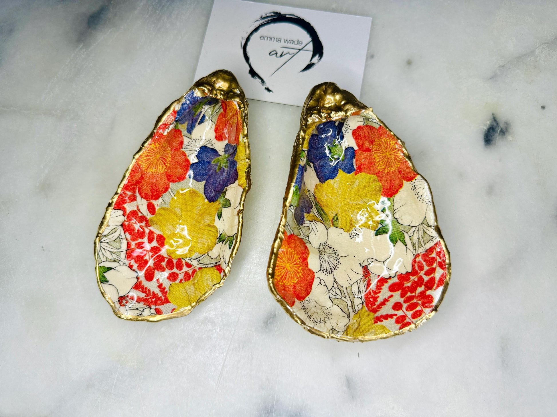 Handmade oyster shell trinket dish featuring a colourful Japanese kimono-style floral design applied with decoupage, finished with hand-gilded gold leaf edges and sealed in glossy clear resin. Natural Dorset oyster shell used as a jewellery dish or ring holder, photographed on a light surface, showcasing the vibrant flowers and luxury gold detailing. Ideal as coastal home decor or a unique handmade gift.