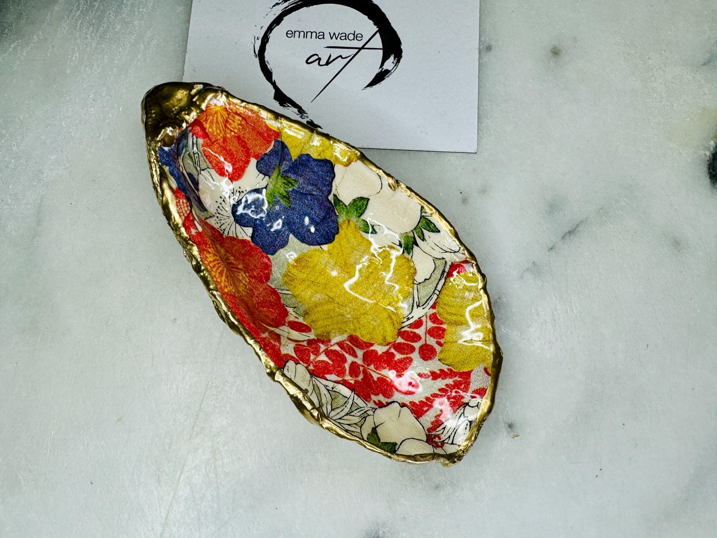 Handmade oyster shell trinket dish featuring a colourful Japanese kimono-style floral design applied with decoupage, finished with hand-gilded gold leaf edges and sealed in glossy clear resin. Natural Dorset oyster shell used as a jewellery dish or ring holder, photographed on a light surface, showcasing the vibrant flowers and luxury gold detailing. Ideal as coastal home decor or a unique handmade gift.