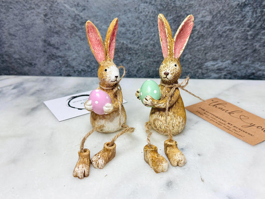 Hand-finished shelf sitting polyresin rabbit ornament with dangling jute legs and polka dot egg. Available with either  pink or green dotty eggs. Perfect Easter rabbit shelf decoration, birthday gift, or home décor accessory. Cute animal figurine for rabbit lovers, Easter decorations, new home presents, or seasonal mantel styling.