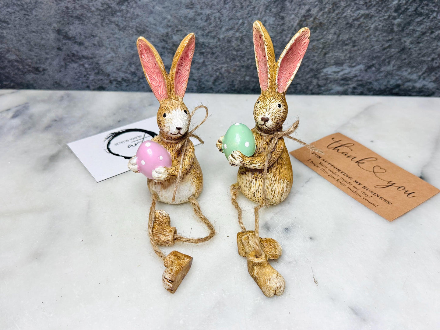 Hand-finished shelf sitting bunny ornament with dangling jute legs and polka dot egg. Available in pink or green. Perfect Easter rabbit shelf decoration, birthday gift, or home décor accessory. Cute animal figurine for rabbit lovers, Easter decorations, new home presents, or seasonal mantel styling.