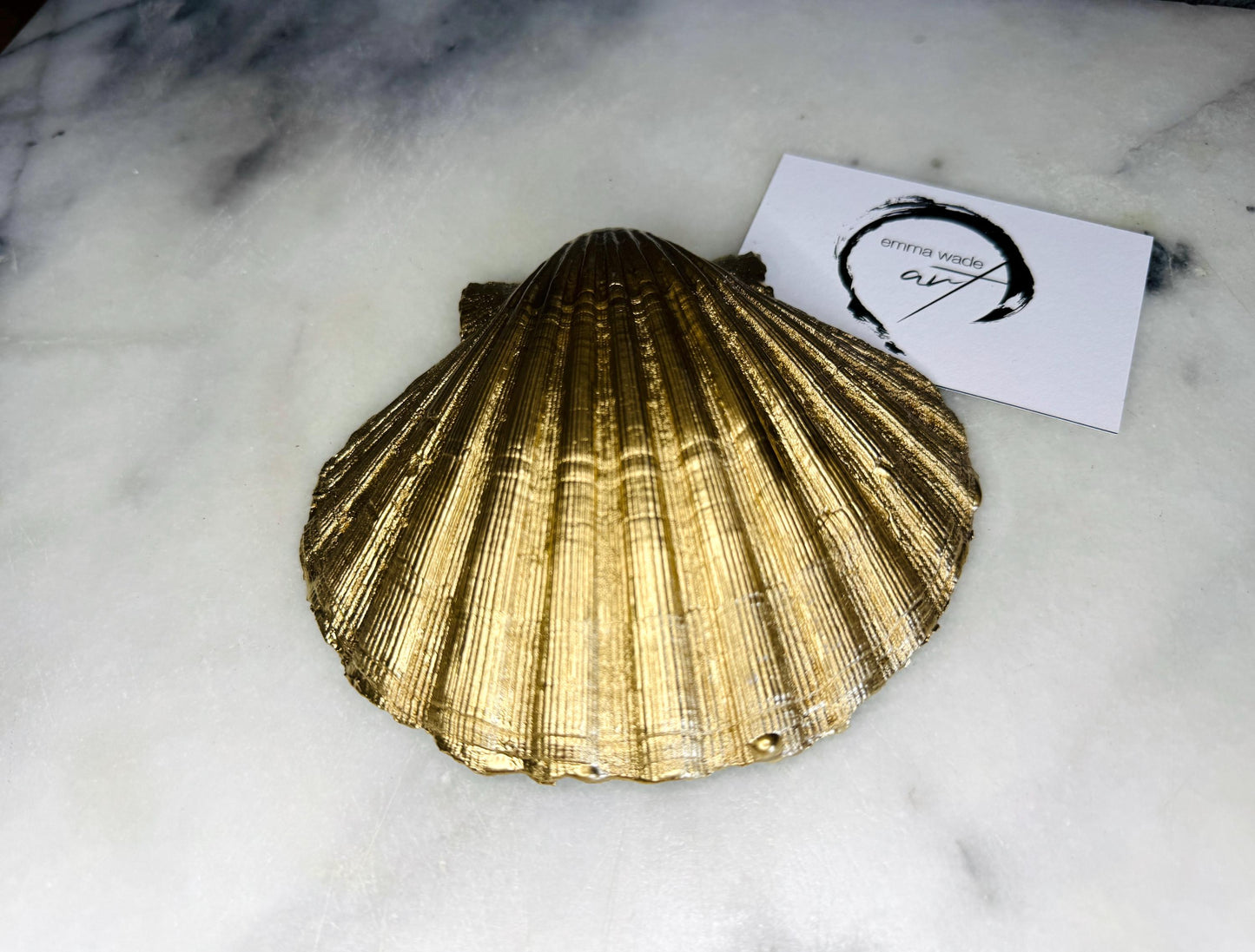 Hand painted blue waves scallop shell trinket dish with gold leaf accents and glossy resin finish, shown with optional gold driftwood display stand. Coastal jewellery and ring dish crafted from a natural Dorset scallop shell, featuring flowing blue wave artwork. Decorative shell bowl photographed on a light background, showing the natural shell shape and gilded edges, ideal for holding rings, earrings, trinkets or small treasures.