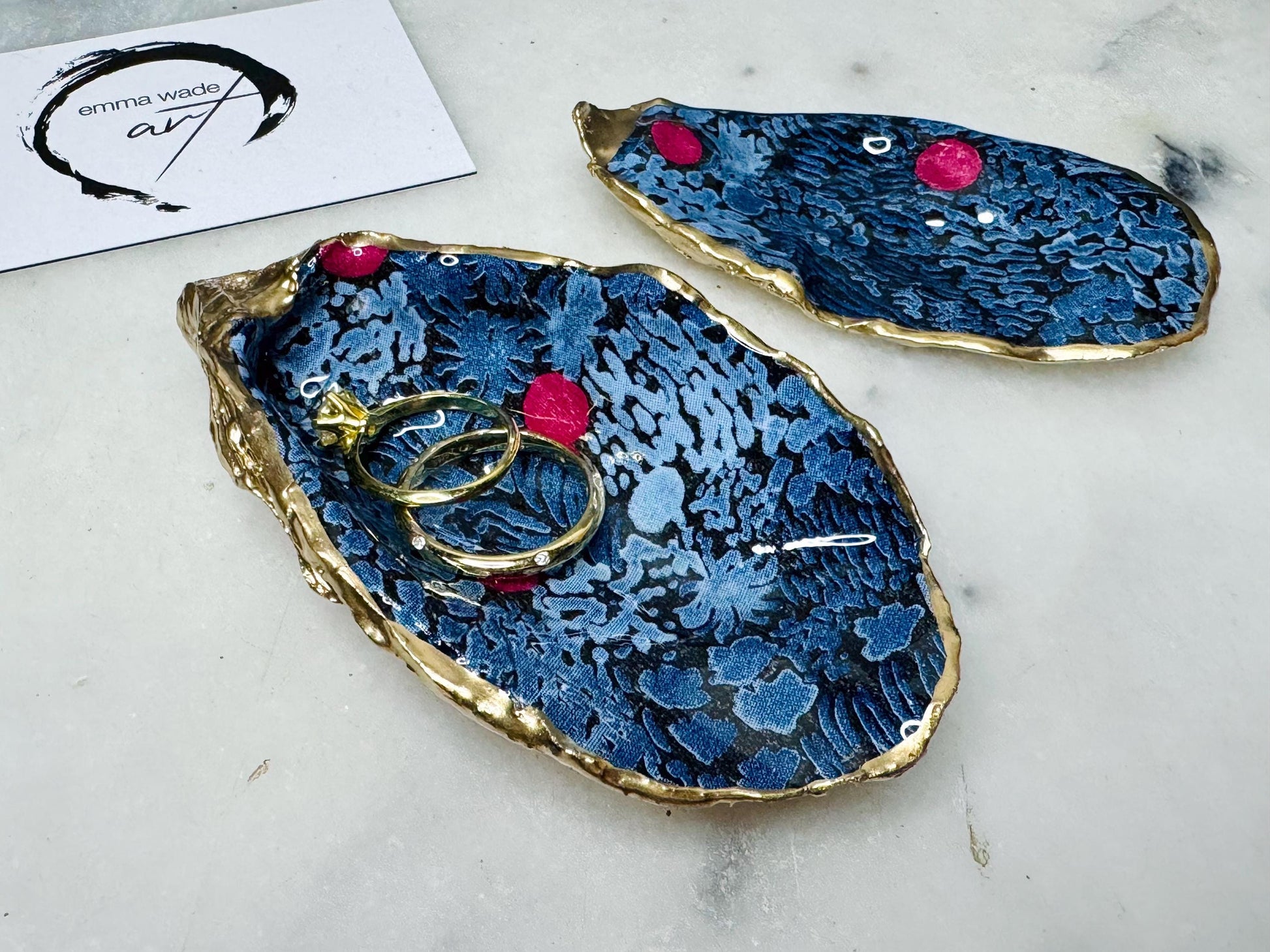 Dorset oyster shell ring box with blue and red Marimekko Kurjenmar decoupage interior and gold leaf exterior, sealed with glossy resin. Natural oyster shell with matching lid, shown holding rings on a light background. Handcrafted coastal jewellery box highlighting the patterned interior, polished edges, and gilded shell back, ideal as an engagement ring box, wedding ring holder, or jewellery keepsake.