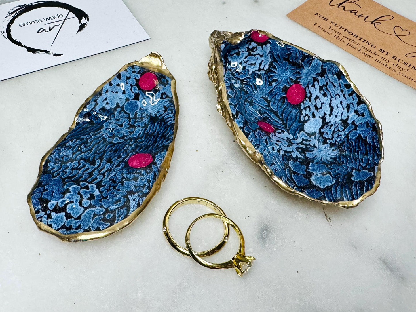 Dorset oyster shell ring box with blue and red Marimekko Kurjenmar decoupage interior and gold leaf exterior, sealed with glossy resin. Natural oyster shell with matching lid, shown holding rings on a light background. Handcrafted coastal jewellery box highlighting the patterned interior, polished edges, and gilded shell back, ideal as an engagement ring box, wedding ring holder, or jewellery keepsake.