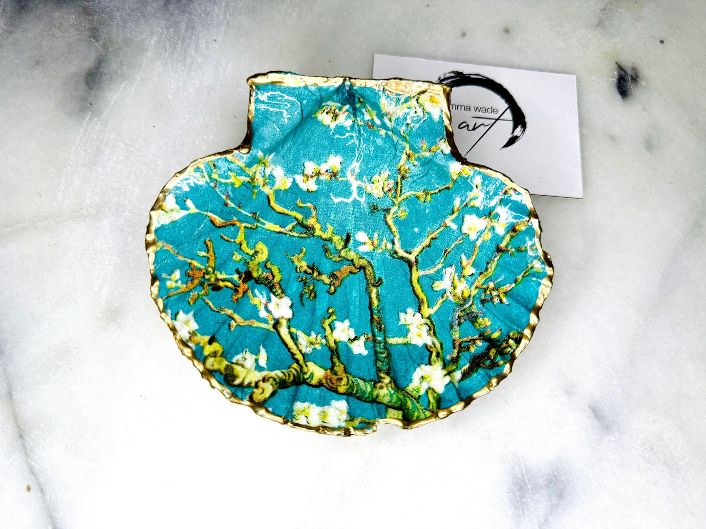 Handcrafted Dorset scallop shell trinket dish inspired by Vincent van Gogh’s Almond Blossom painting. Turquoise blue and green background with branching blossom design and raised gold detailing, finished with liquid gold leaf edging and sealed in high-gloss resin. Decorative shell jewellery holder styled on marble surface, suitable for rings, earrings, trinkets or as a tea light holder. Coastal art-inspired home decor piece.