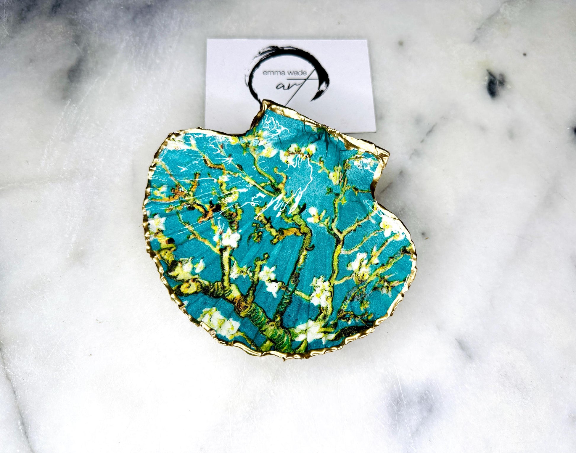 Handcrafted Dorset scallop shell trinket dish inspired by Vincent van Gogh’s Almond Blossom painting. Turquoise blue and green background with branching blossom design and raised gold detailing, finished with liquid gold leaf edging and sealed in high-gloss resin. Decorative shell jewellery holder styled on marble surface, suitable for rings, earrings, trinkets or as a tea light holder. Coastal art-inspired home decor piece.