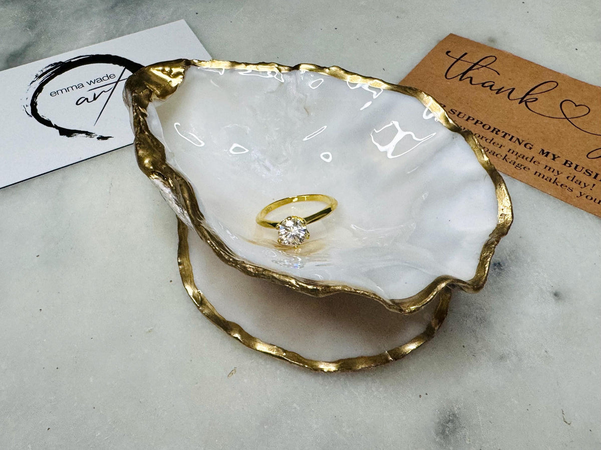 Handcrafted Dorset oyster shell ring box with matching natural shell lid, featuring a luminous inset Swarovski pearl nestled inside the cupped shell. Interior has a soft pearlescent white sheen and is sealed with crystal-clear resin. Optional outer finish in natural pearl tone or pearl with subtle gold leaf highlights. Coastal-inspired engagement proposal ring holder and wedding keepsake, styled on marble surface.