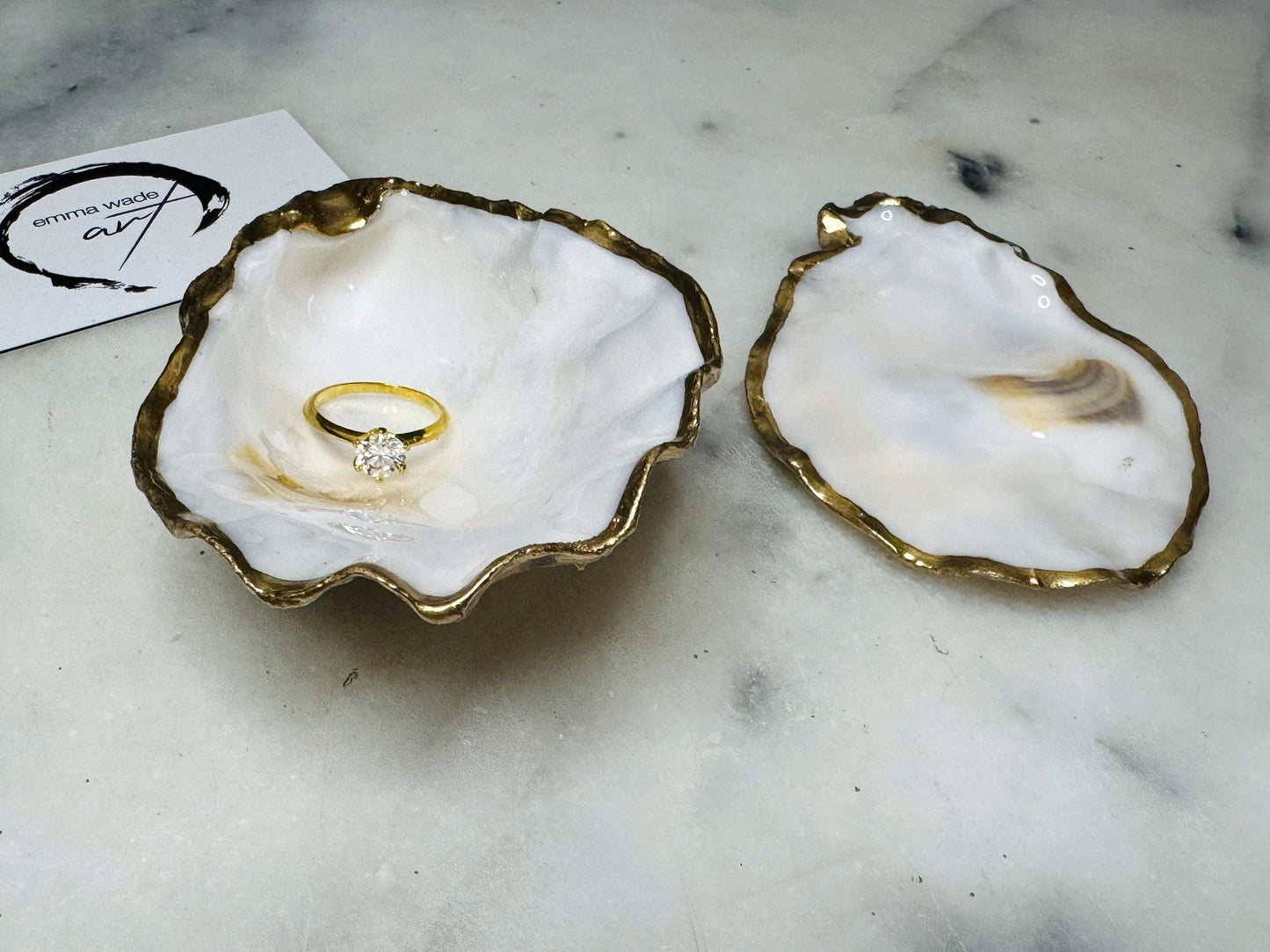 Handcrafted Dorset oyster shell ring box with matching natural shell lid, featuring a luminous inset Swarovski pearl nestled inside the cupped shell. Interior has a soft pearlescent white sheen and is sealed with crystal-clear resin. Optional outer finish in natural pearl tone or pearl with subtle gold leaf highlights. Coastal-inspired engagement proposal ring holder and wedding keepsake, styled on marble surface.