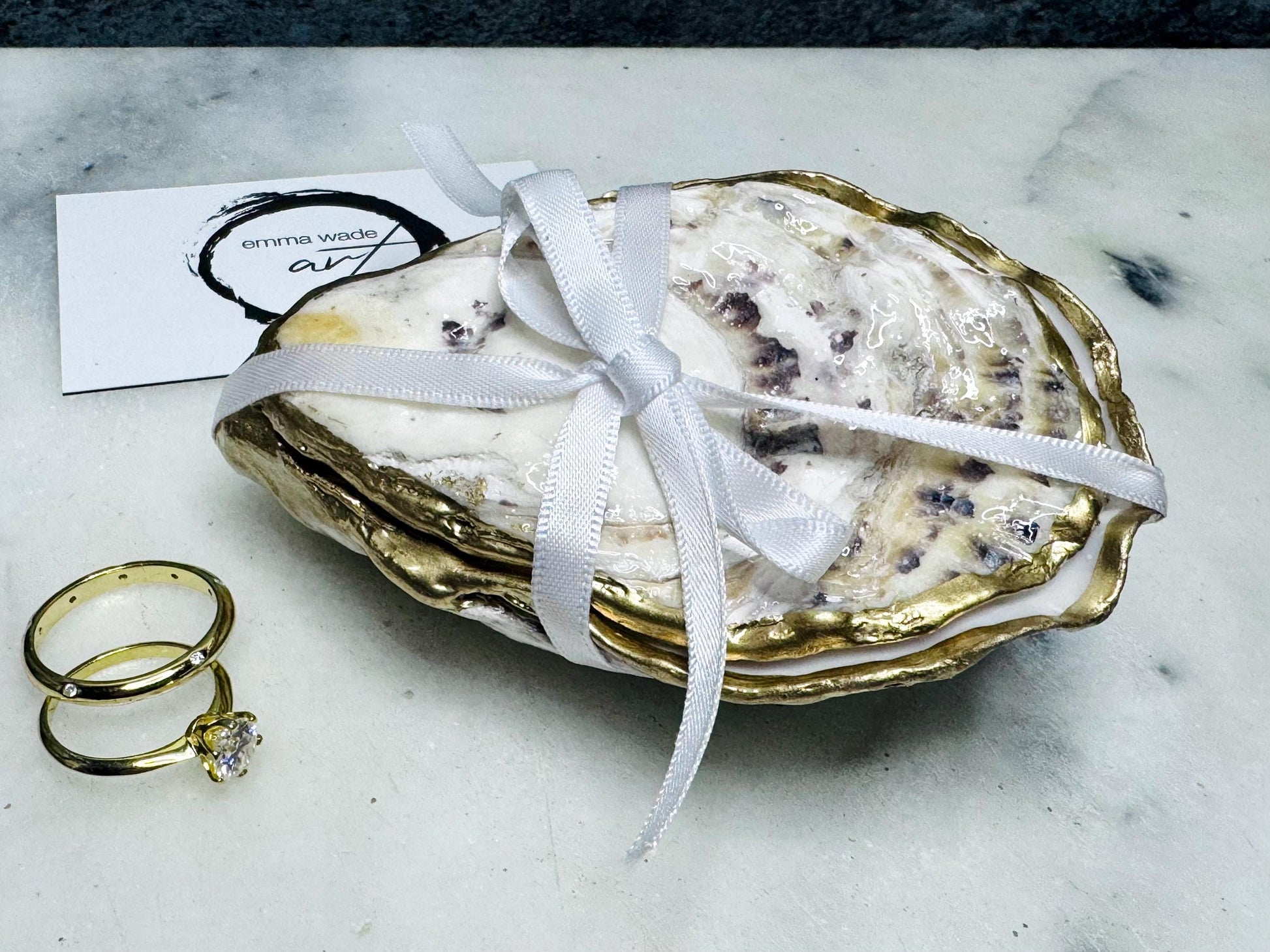Handcrafted Dorset oyster shell ring box with matching natural shell lid, featuring a luminous inset Swarovski pearl nestled inside the cupped shell. Interior has a soft pearlescent white sheen and is sealed with crystal-clear resin. Optional outer finish in natural pearl tone or pearl with subtle gold leaf highlights. Coastal-inspired engagement proposal ring holder and wedding keepsake, styled on marble surface.