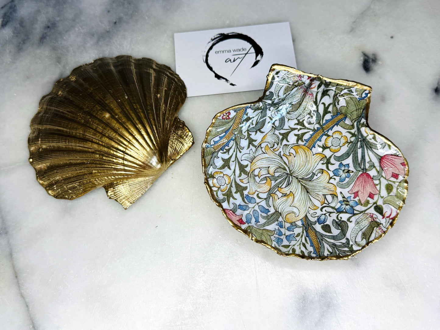 Handcrafted Dorset scallop shell trinket dish featuring William Morris Golden Lily floral design. Natural shell edged with hand applied gold leaf and sealed with glossy resin. Heritage floral jewellery holder displayed with rings on marble surface. Elegant coastal home decor gift.