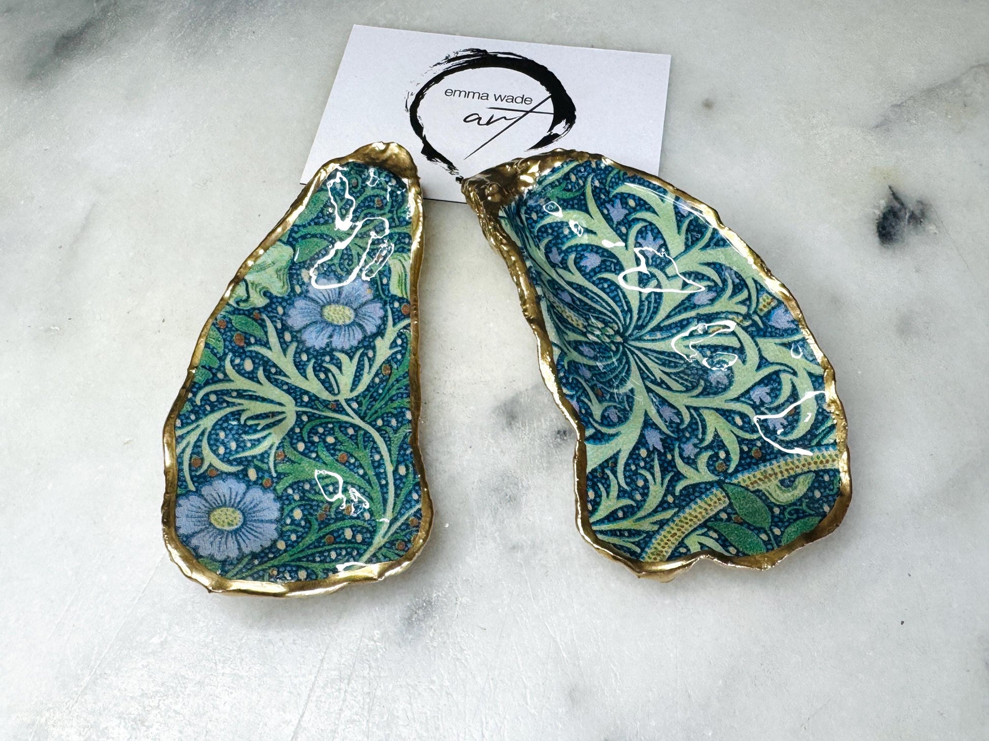 Handmade William Morris inspired oyster shell trinket dish in green and blue tones, finished with gold leaf and sealed with glossy resin. Coastal jewellery dish made from a Dorset oyster shell, featuring a seaweed decoupage design. Perfect for holding rings, earrings and small treasures. Decorative shell bowl photographed on a light background, showing the natural shell shape, detailed pattern and gilded edges.