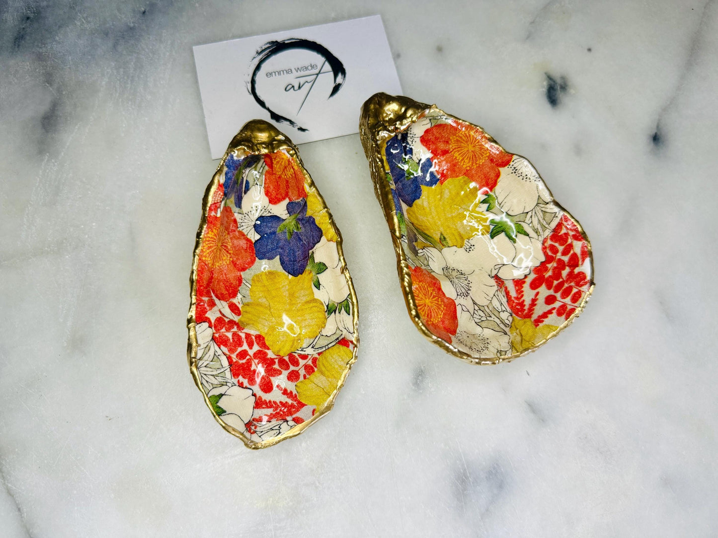 Handmade oyster shell trinket dish featuring a colourful Japanese kimono-style floral design applied with decoupage, finished with hand-gilded gold leaf edges and sealed in glossy clear resin. Natural Dorset oyster shell used as a jewellery dish or ring holder, photographed on a light surface, showcasing the vibrant flowers and luxury gold detailing. Ideal as coastal home decor or a unique handmade gift.