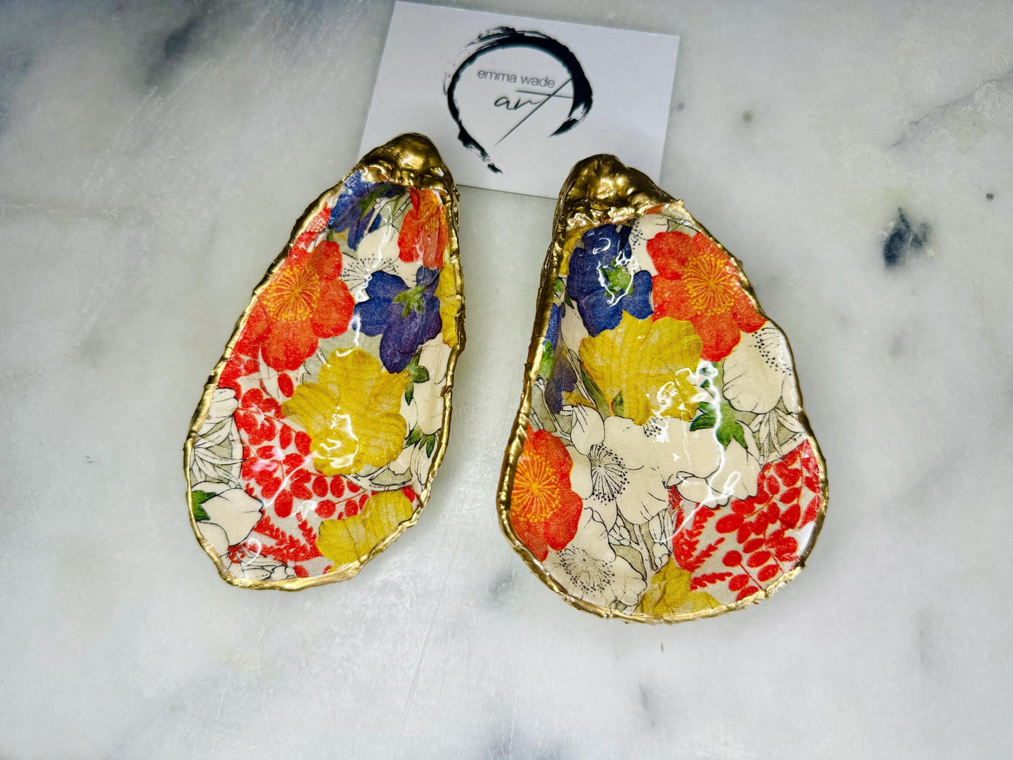 Handmade oyster shell trinket dish featuring a colourful Japanese kimono-style floral design applied with decoupage, finished with hand-gilded gold leaf edges and sealed in glossy clear resin. Natural Dorset oyster shell used as a jewellery dish or ring holder, photographed on a light surface, showcasing the vibrant flowers and luxury gold detailing. Ideal as coastal home decor or a unique handmade gift.