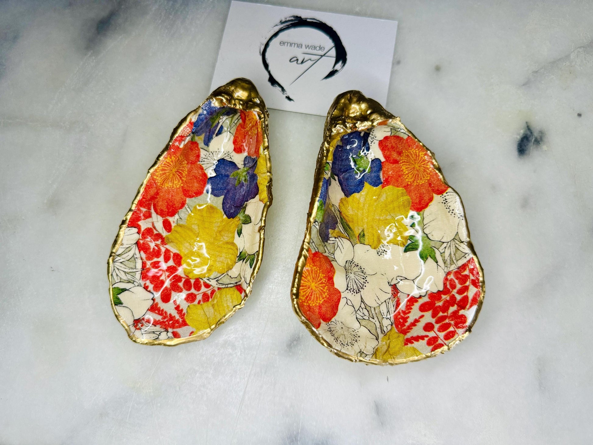 Handmade oyster shell trinket dish featuring a colourful Japanese kimono-style floral design applied with decoupage, finished with hand-gilded gold leaf edges and sealed in glossy clear resin. Natural Dorset oyster shell used as a jewellery dish or ring holder, photographed on a light surface, showcasing the vibrant flowers and luxury gold detailing. Ideal as coastal home decor or a unique handmade gift.