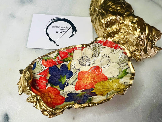 Handmade oyster shell trinket dish featuring a colourful Japanese kimono-style floral design applied with decoupage, finished with hand-gilded gold leaf edges and sealed in glossy clear resin. Natural Dorset oyster shell used as a jewellery dish or ring holder, photographed on a light surface, showcasing the vibrant flowers and luxury gold detailing. Ideal as coastal home decor or a unique handmade gift.