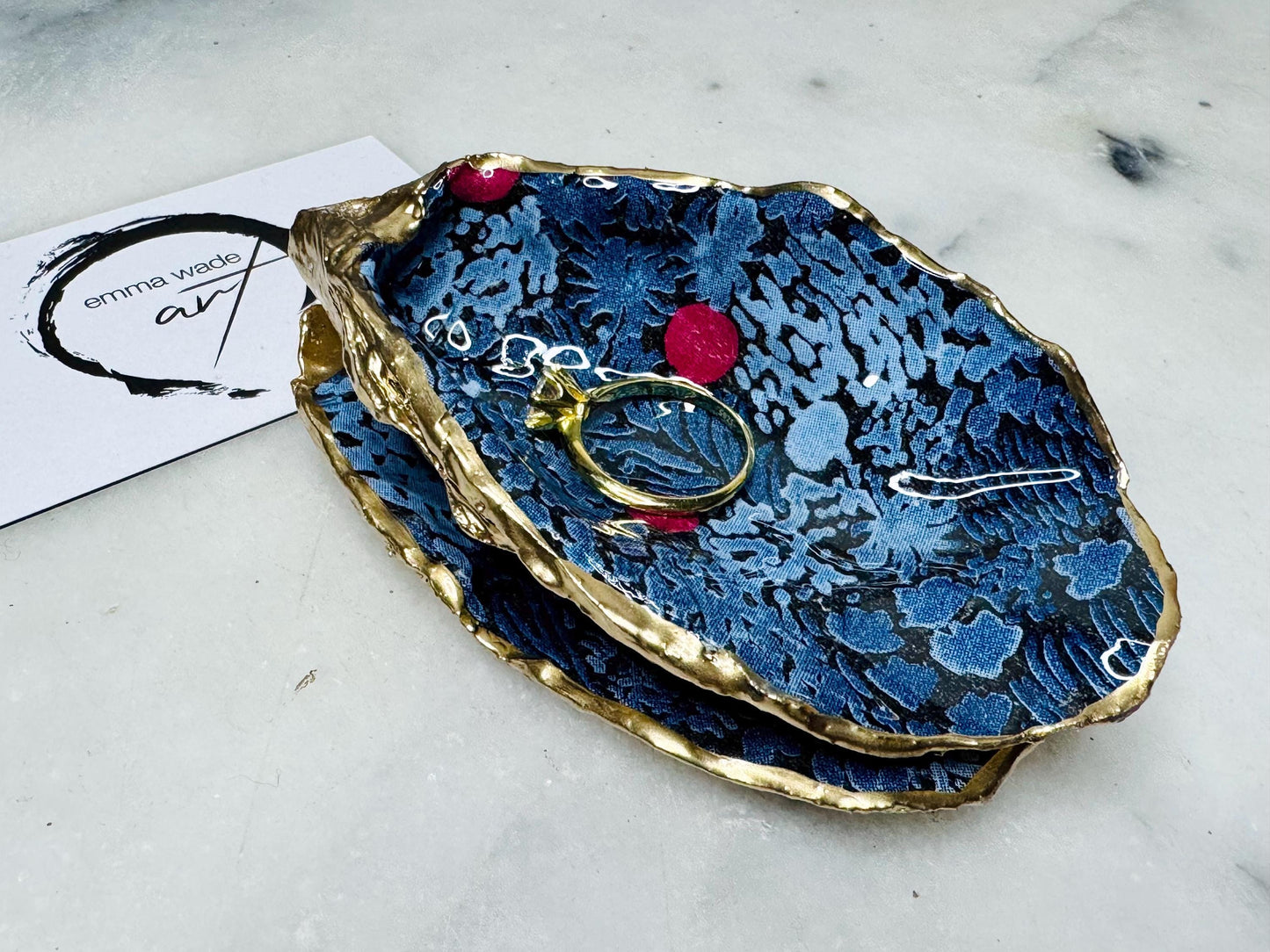 Dorset oyster shell ring box with blue and red Marimekko Kurjenmar decoupage interior and gold leaf exterior, sealed with glossy resin. Natural oyster shell with matching lid, shown holding rings on a light background. Handcrafted coastal jewellery box highlighting the patterned interior, polished edges, and gilded shell back, ideal as an engagement ring box, wedding ring holder, or jewellery keepsake.