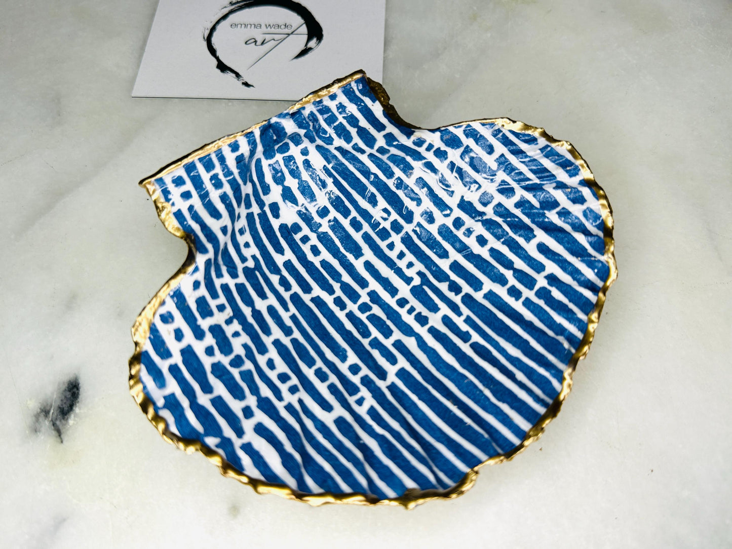 Handmade blue and white scallop shell trinket dish with gold leaf edging, crafted from a genuine Dorset shell and sealed with glossy resin. Coastal ring dish and jewellery holder featuring elegant blue line design, displayed in gift packaging. Artisan shell decor handmade in Surrey, perfect for coastal home styling, wedding gifts or nautical themed interiors.