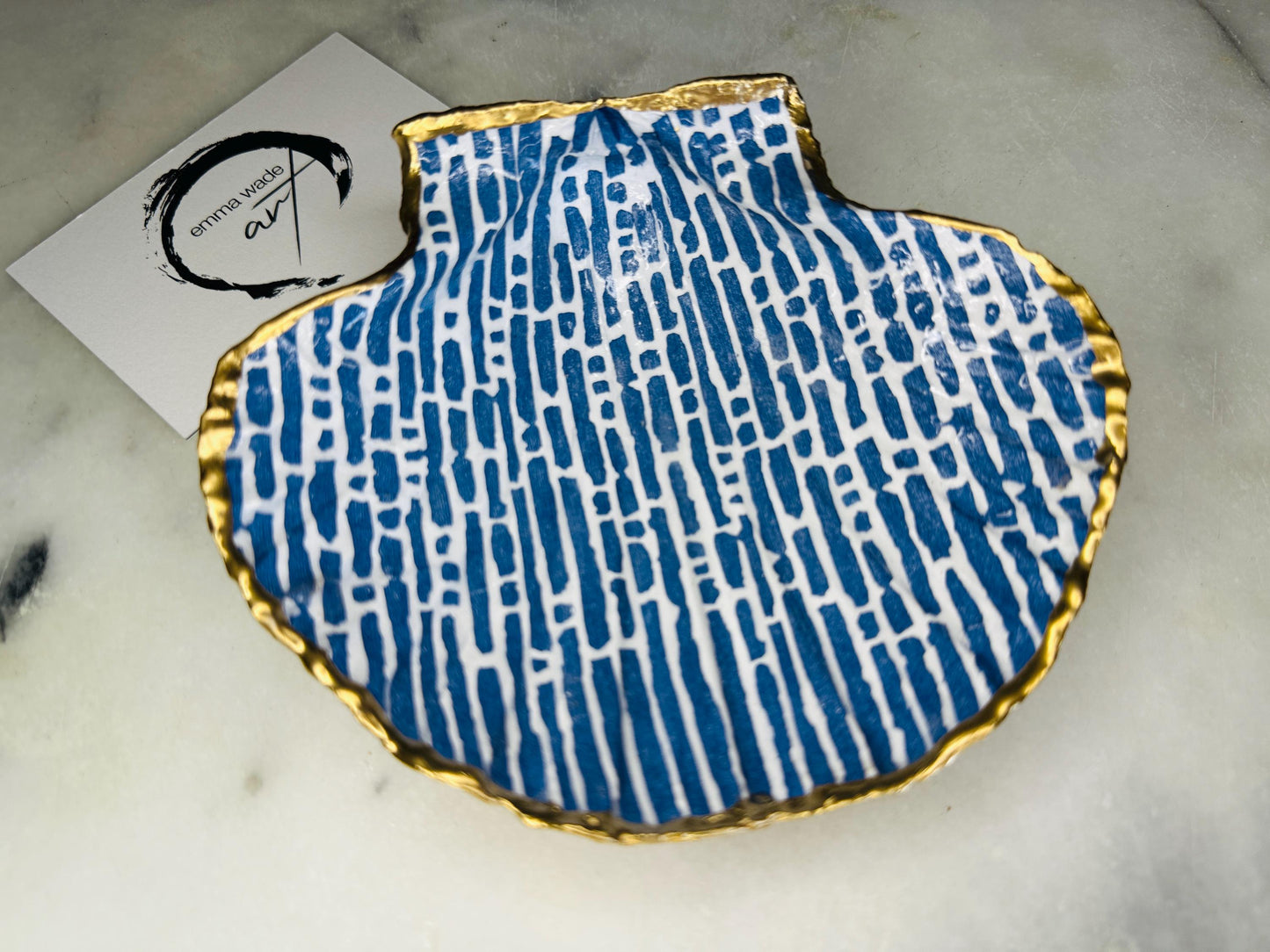 Handmade blue and white scallop shell trinket dish with gold leaf edging, crafted from a genuine Dorset shell and sealed with glossy resin. Coastal ring dish and jewellery holder featuring elegant blue line design, displayed in gift packaging. Artisan shell decor handmade in Surrey, perfect for coastal home styling, wedding gifts or nautical themed interiors.