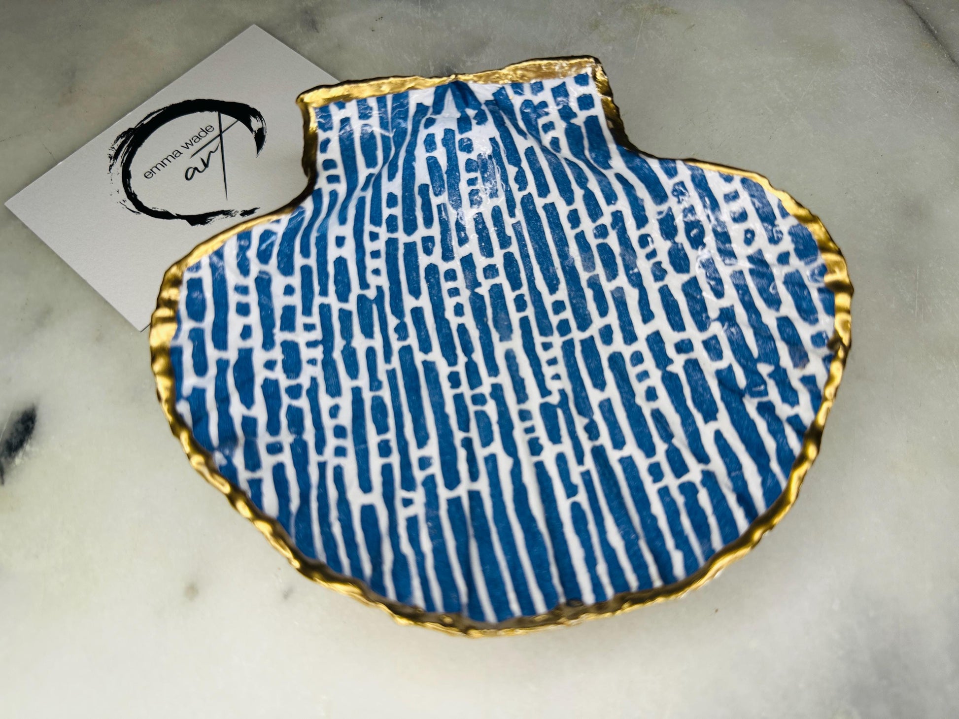 Handmade blue and white scallop shell trinket dish with gold leaf edging, crafted from a genuine Dorset shell and sealed with glossy resin. Coastal ring dish and jewellery holder featuring elegant blue line design, displayed in gift packaging. Artisan shell decor handmade in Surrey, perfect for coastal home styling, wedding gifts or nautical themed interiors.